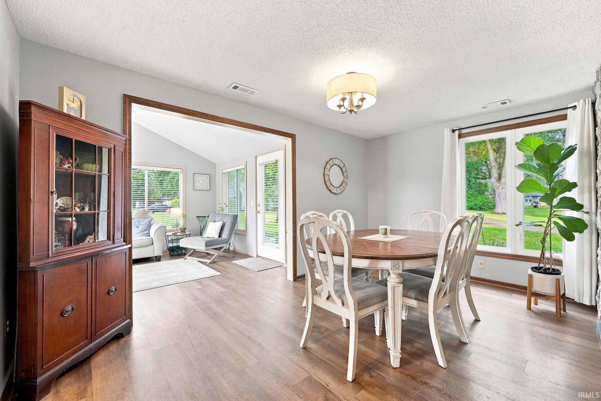 Spacious dining area featuring wood-finish flooring, a contemporary ceiling light fixture, and a large window with exterior greenery