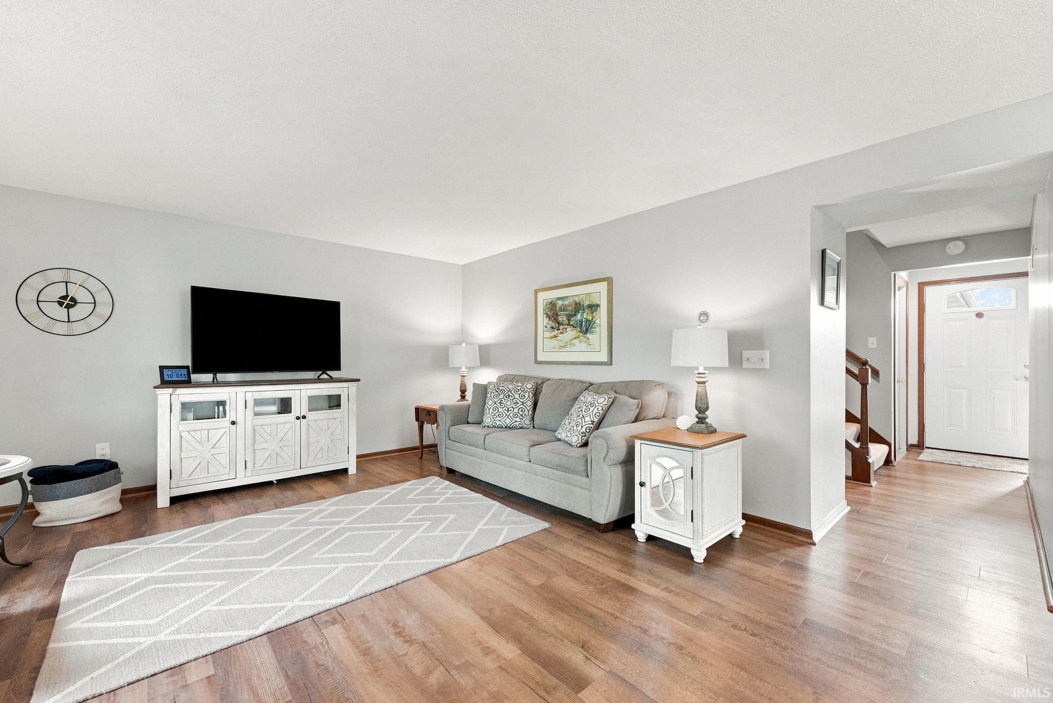 Open-concept living area with wood-finish flooring, light-toned wall paint, and a visible entryway