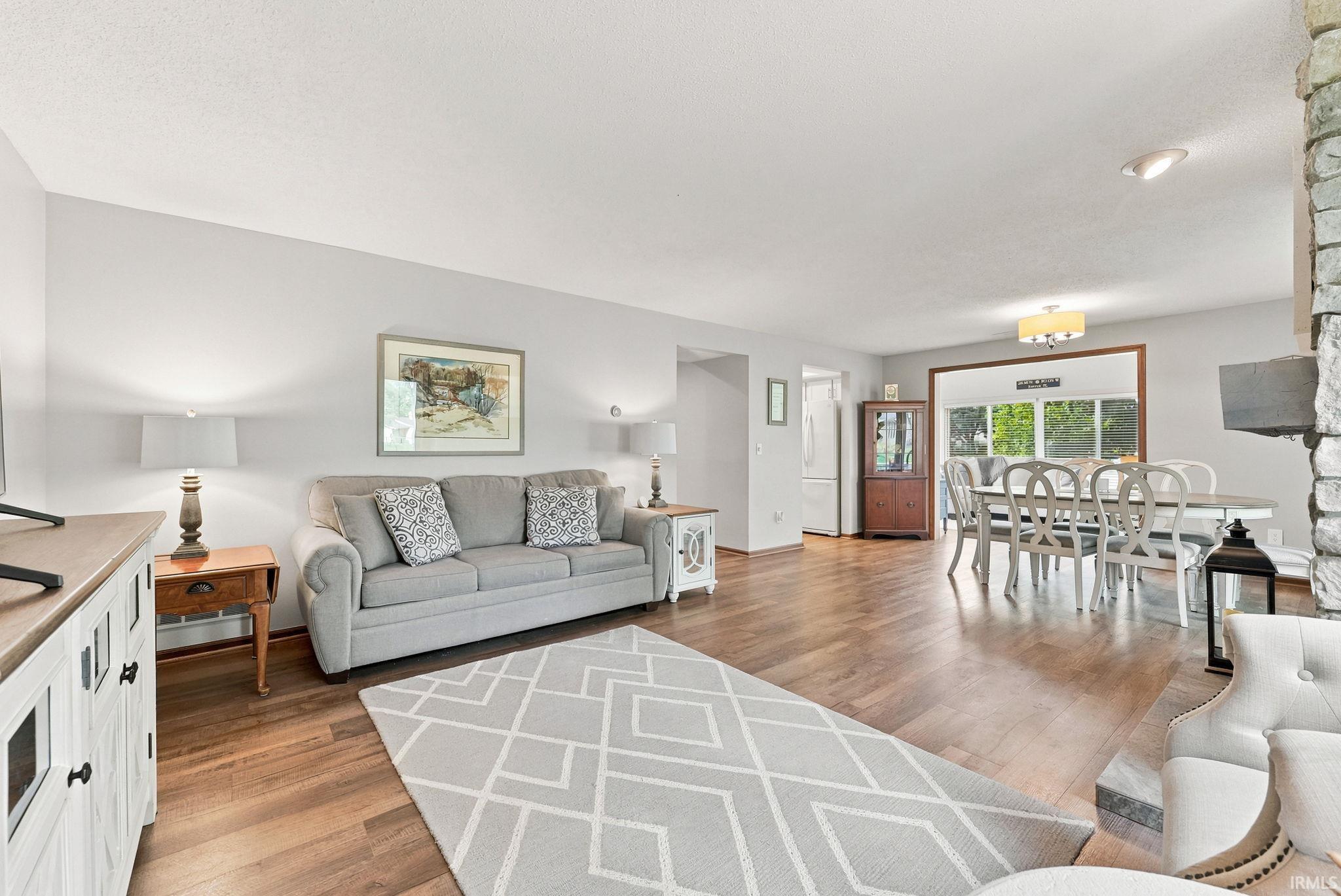 Spacious open-concept living area featuring wood-finish flooring, light gray wall tones, and a prominent stone fireplace surround