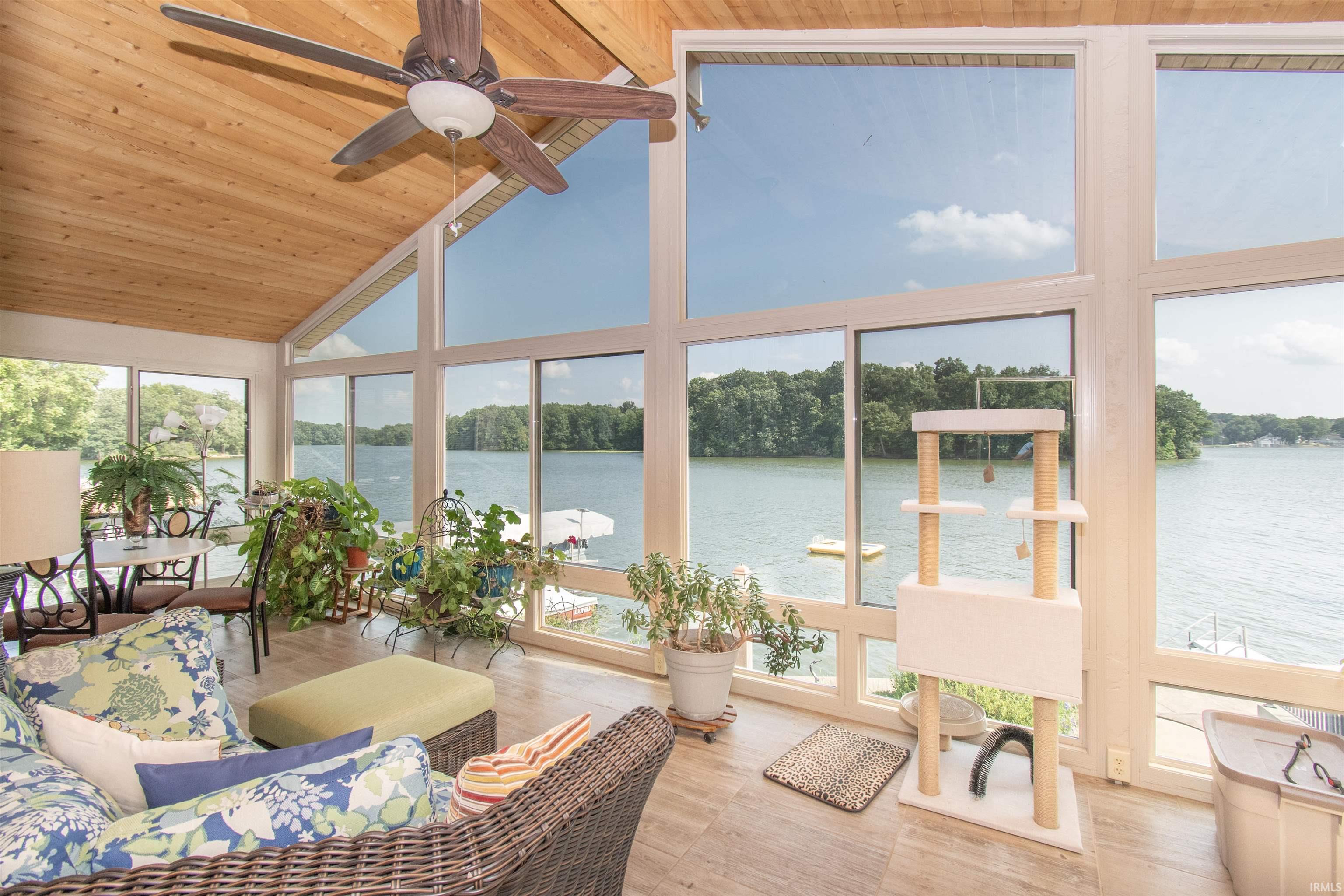 Sunroom featuring a vaulted wood-finish ceiling with a ceiling fan, extensive windows providing water frontage, wood-finish flooring, and ample natural light