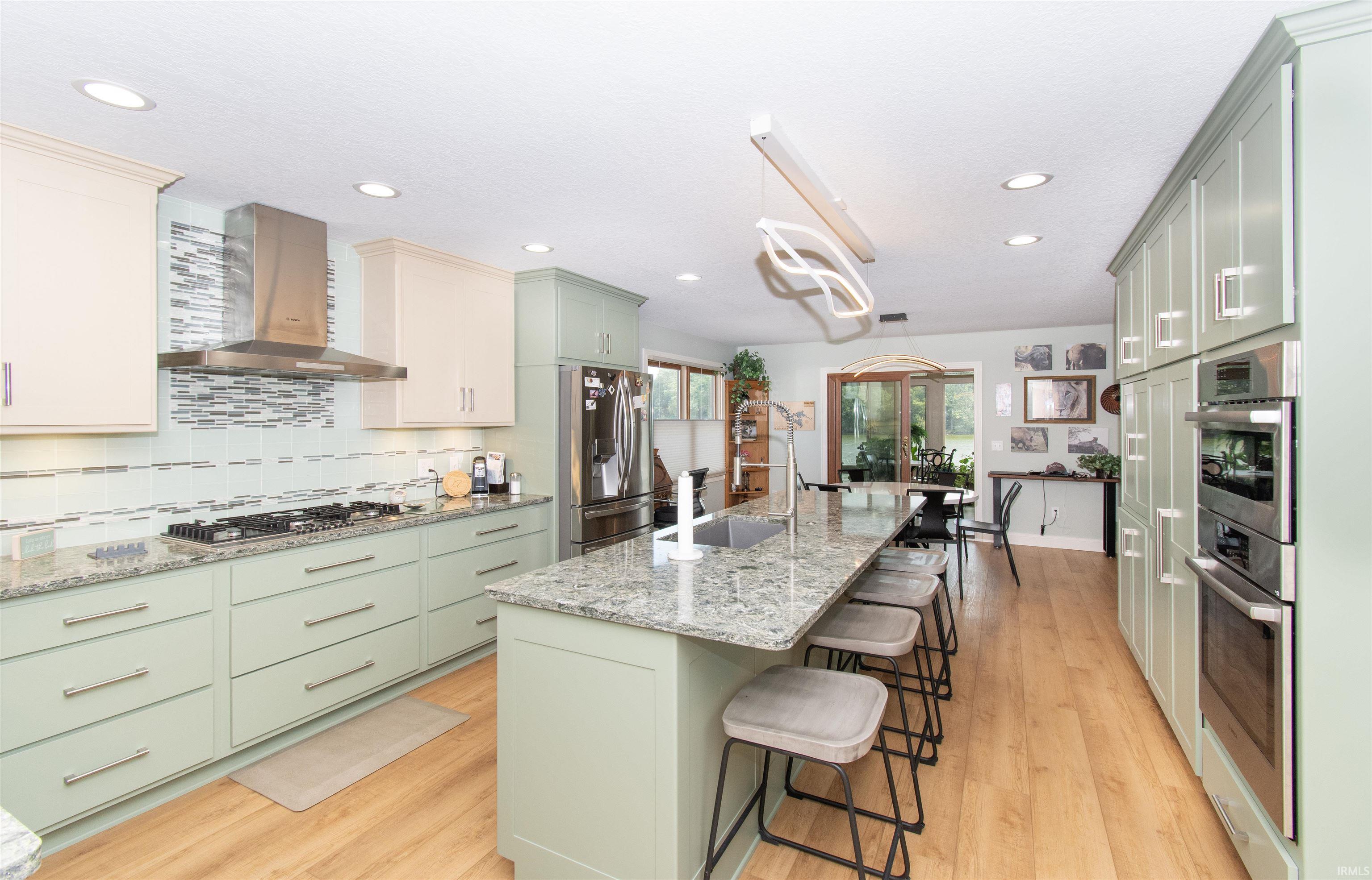 Spacious kitchen featuring an extended island with seating, light wood-finish flooring, two-tone cabinetry, stainless steel appliances, and recessed lighting