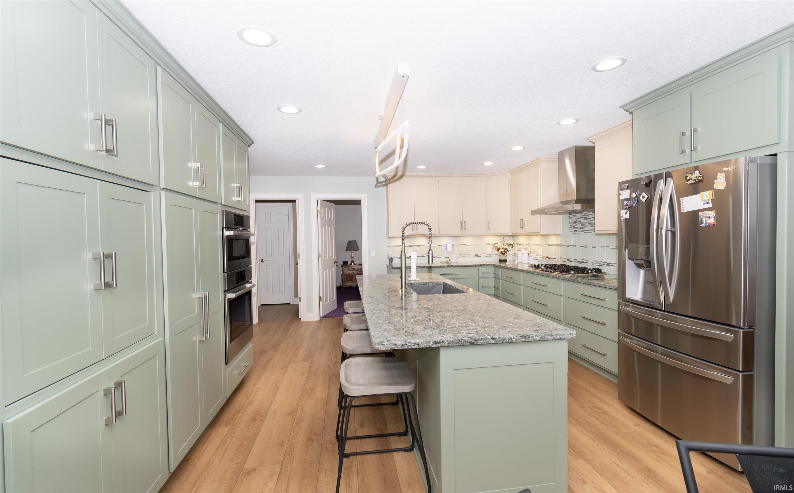 Spacious kitchen featuring an expansive center island with seating, abundant two-tone cabinetry, stainless steel appliances, wood-finish flooring, and recessed lighting