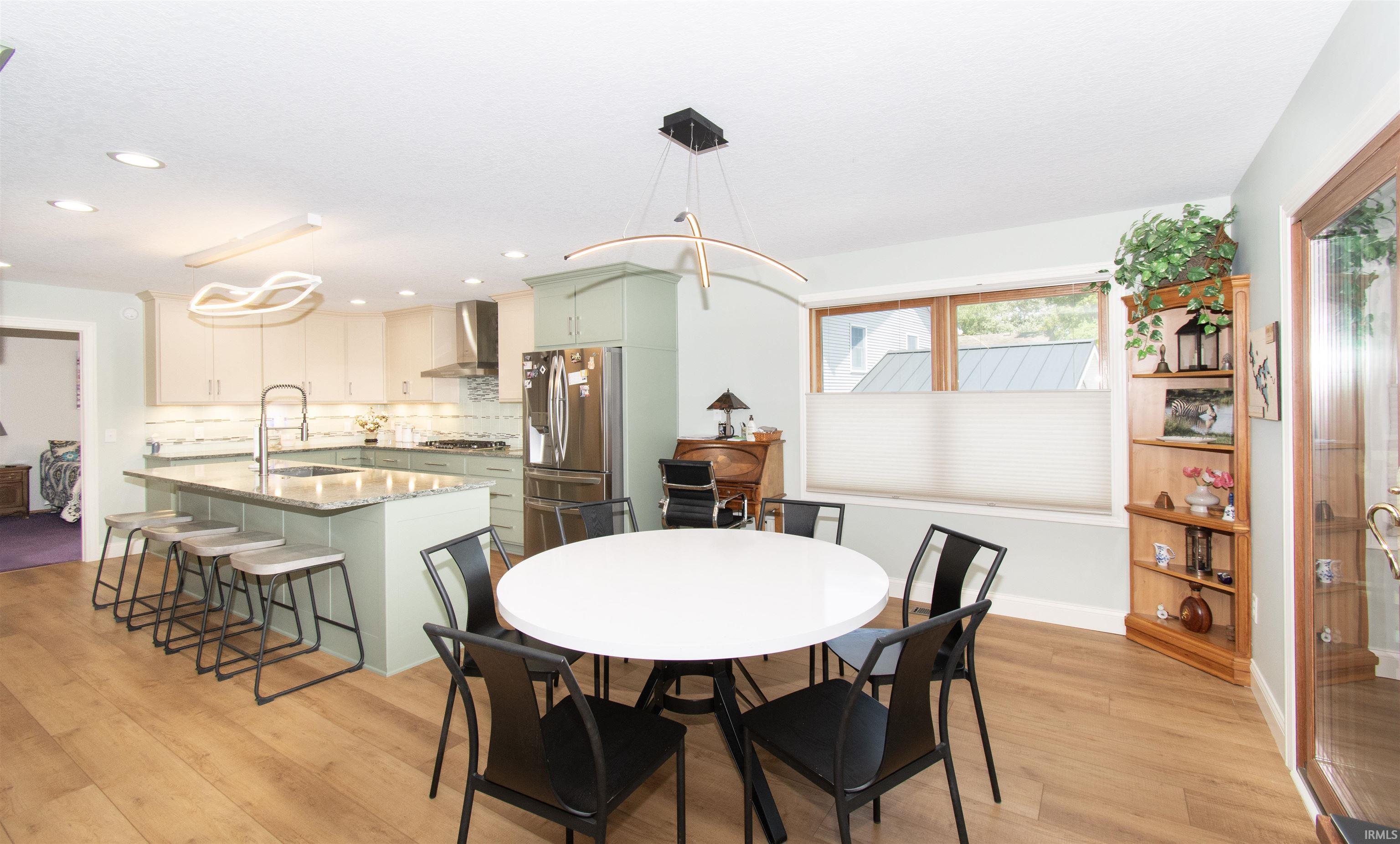 Open-concept living space featuring wood-finish flooring, a kitchen island with seating, stainless steel appliances, modern overhead lighting, and built-in window seating