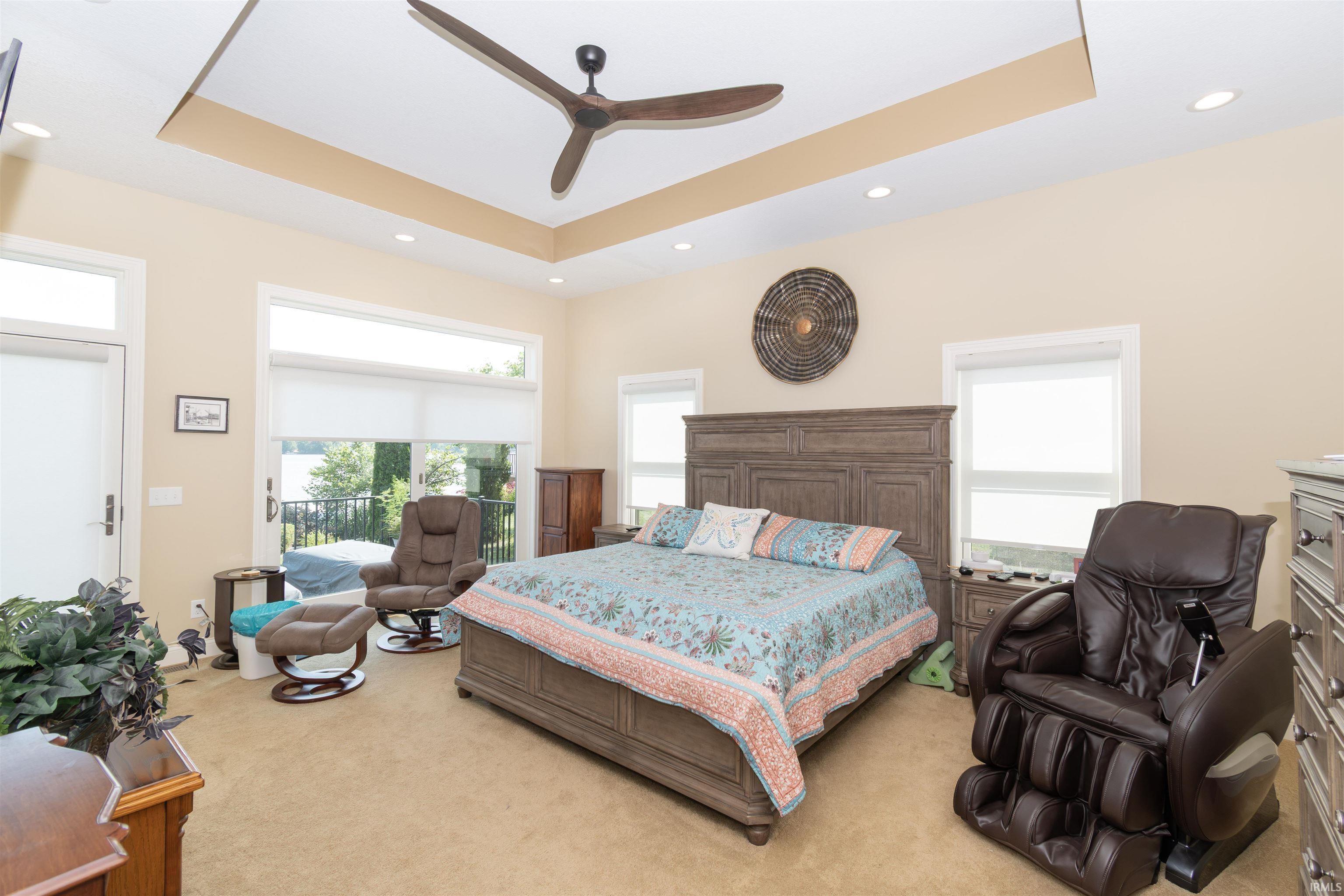 Spacious room featuring a tray ceiling with a modern ceiling fan and recessed lighting, multiple large windows providing ample natural light, a glass-paned door leading to an outdoor area, and soft carpet flooring