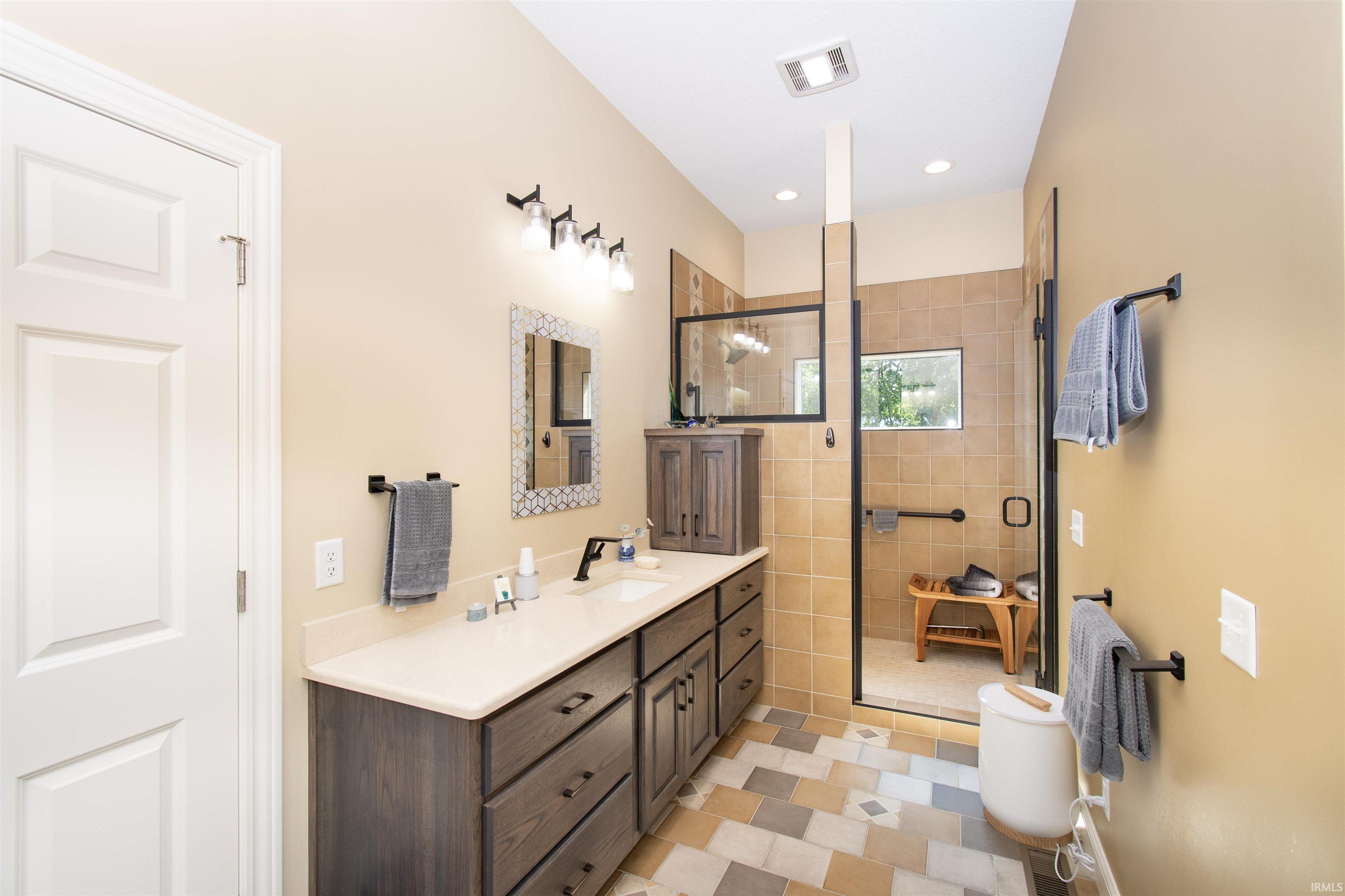 Spacious bathroom featuring a double vanity with stone-finish countertop, wood-finish cabinetry, and a walk-in shower with tile surround