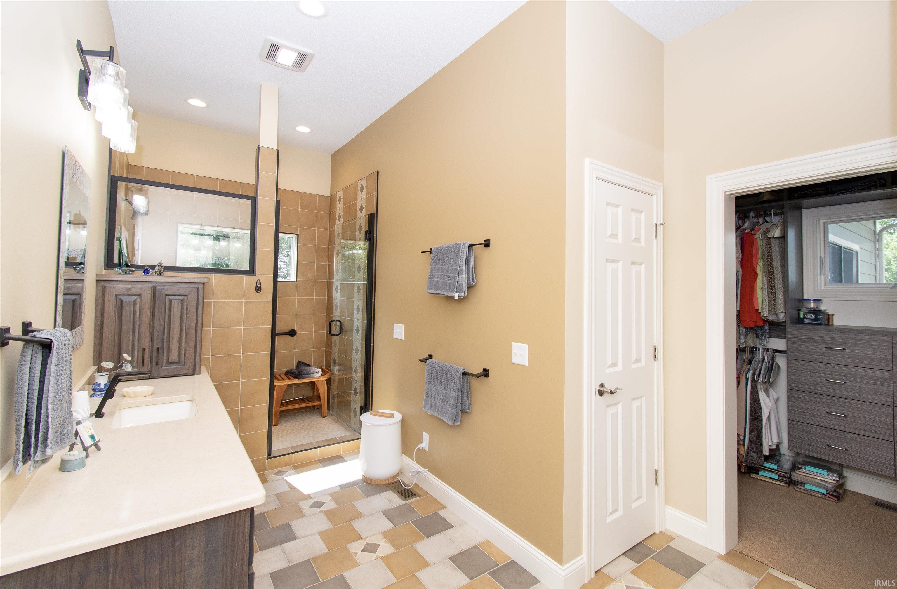 Bathroom featuring a walk-in shower with glass enclosure, single vanity with light-toned countertop, integrated mirrored medicine cabinet, and patterned tile flooring