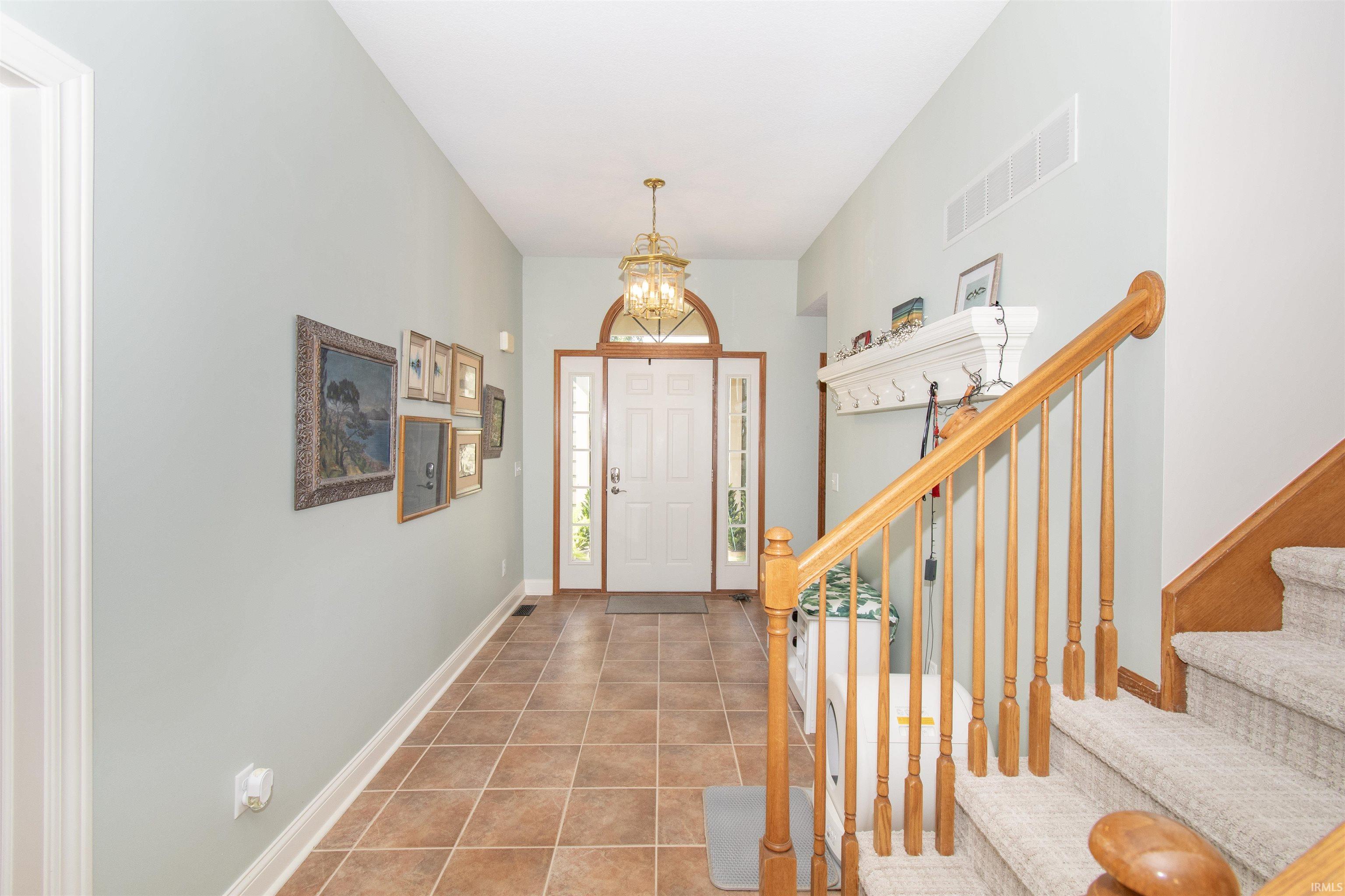 Entry foyer featuring tiled flooring, a front door with sidelights and an arched transom, a brass chandelier, and a wood staircase with carpeted treads