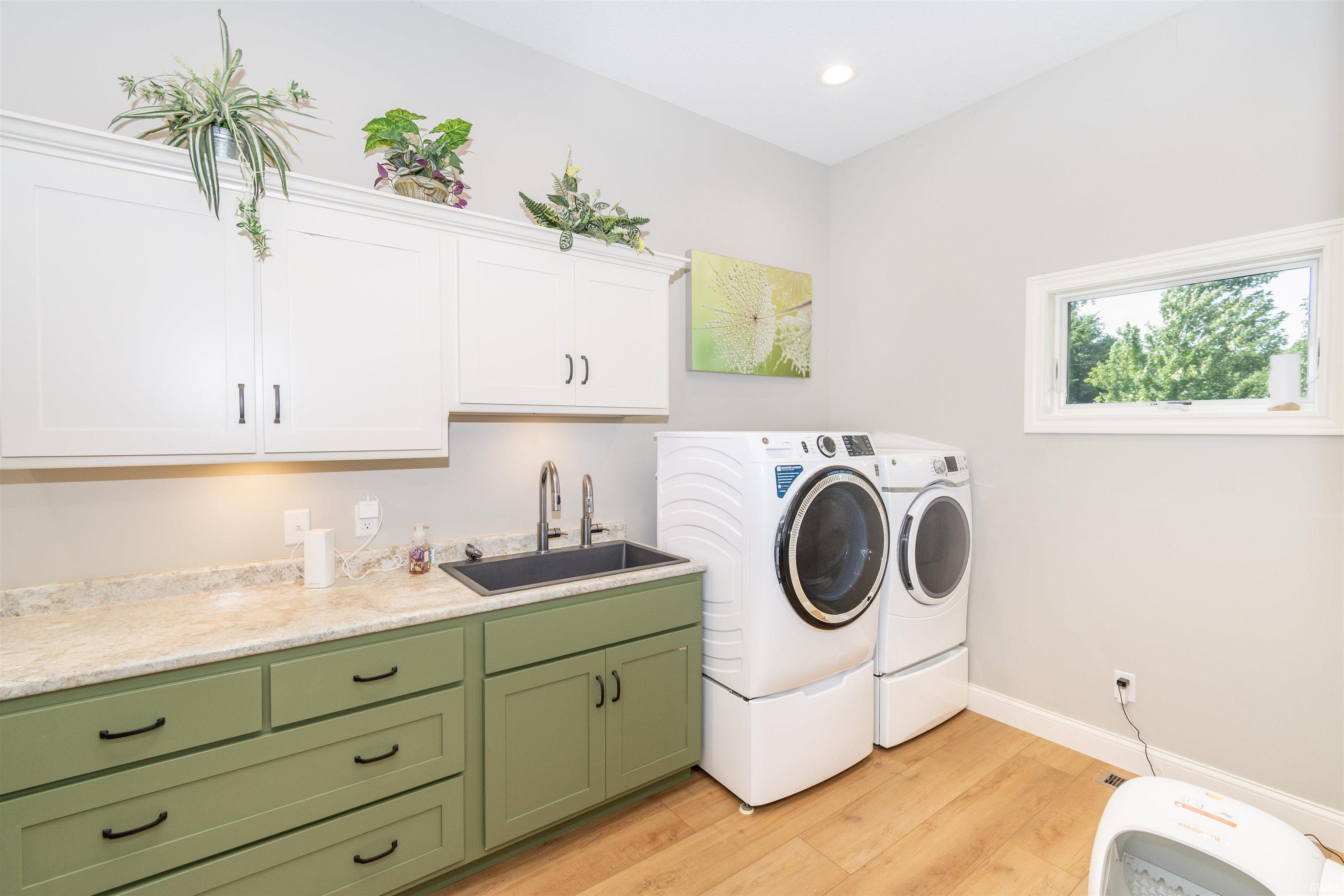Dedicated laundry space featuring extensive cabinetry, an integrated sink, durable countertop, wood-finish flooring, and natural light