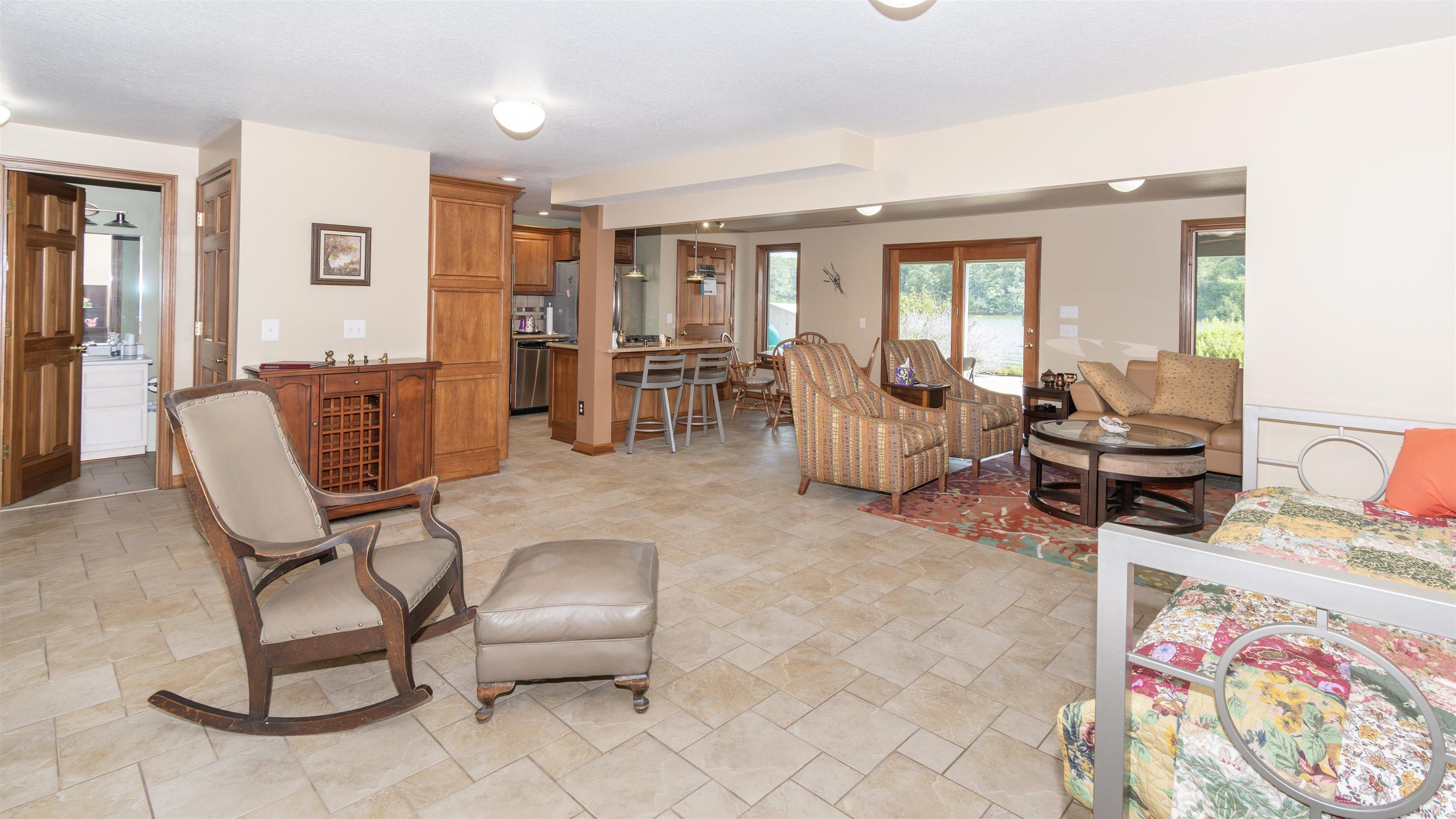 Spacious open-concept area featuring neutral-toned tile flooring, recessed lighting, and a kitchen with wood cabinetry and stainless steel appliances