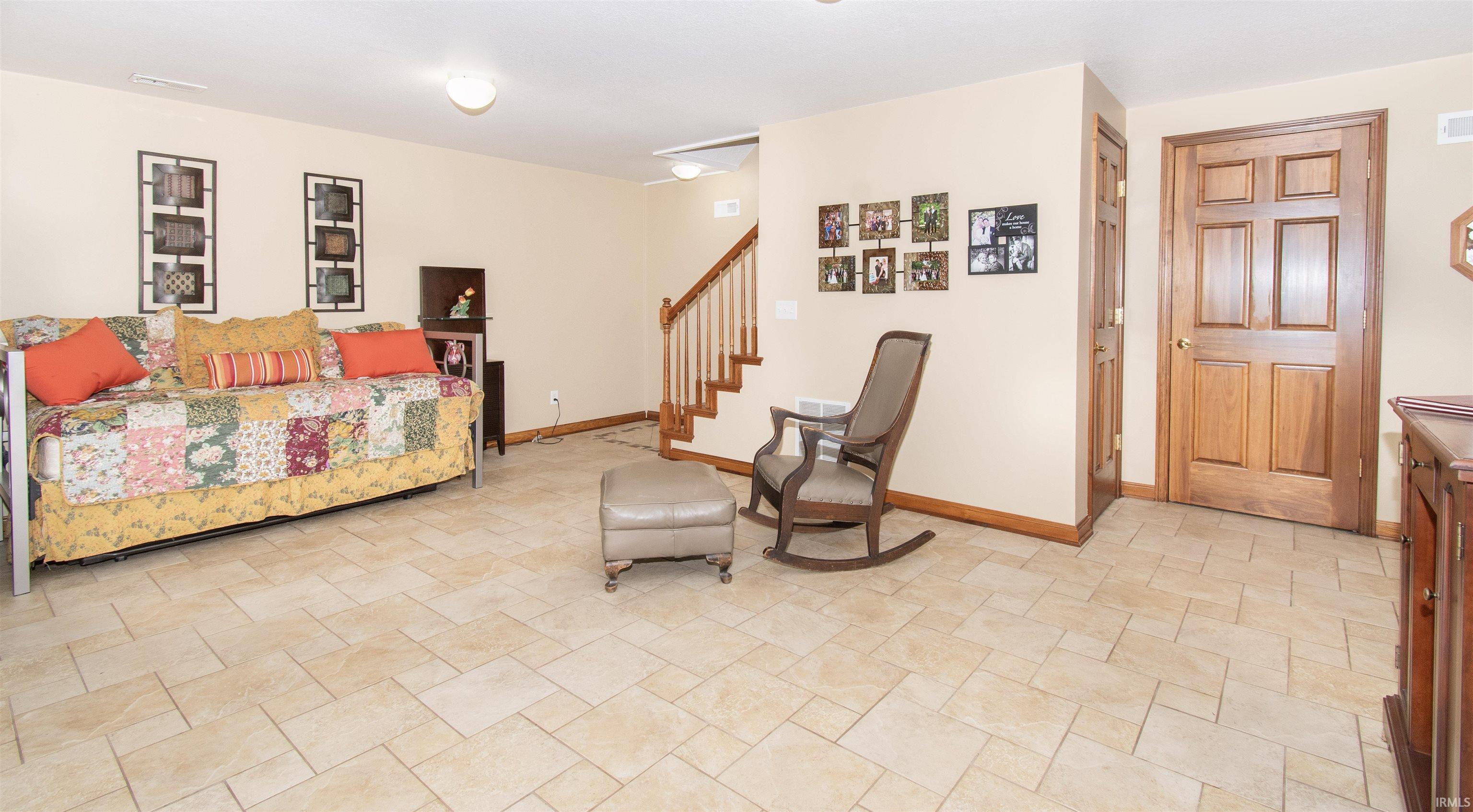 Spacious room featuring neutral-toned tile flooring, light cream wall paint, and a wooden staircase with white balusters