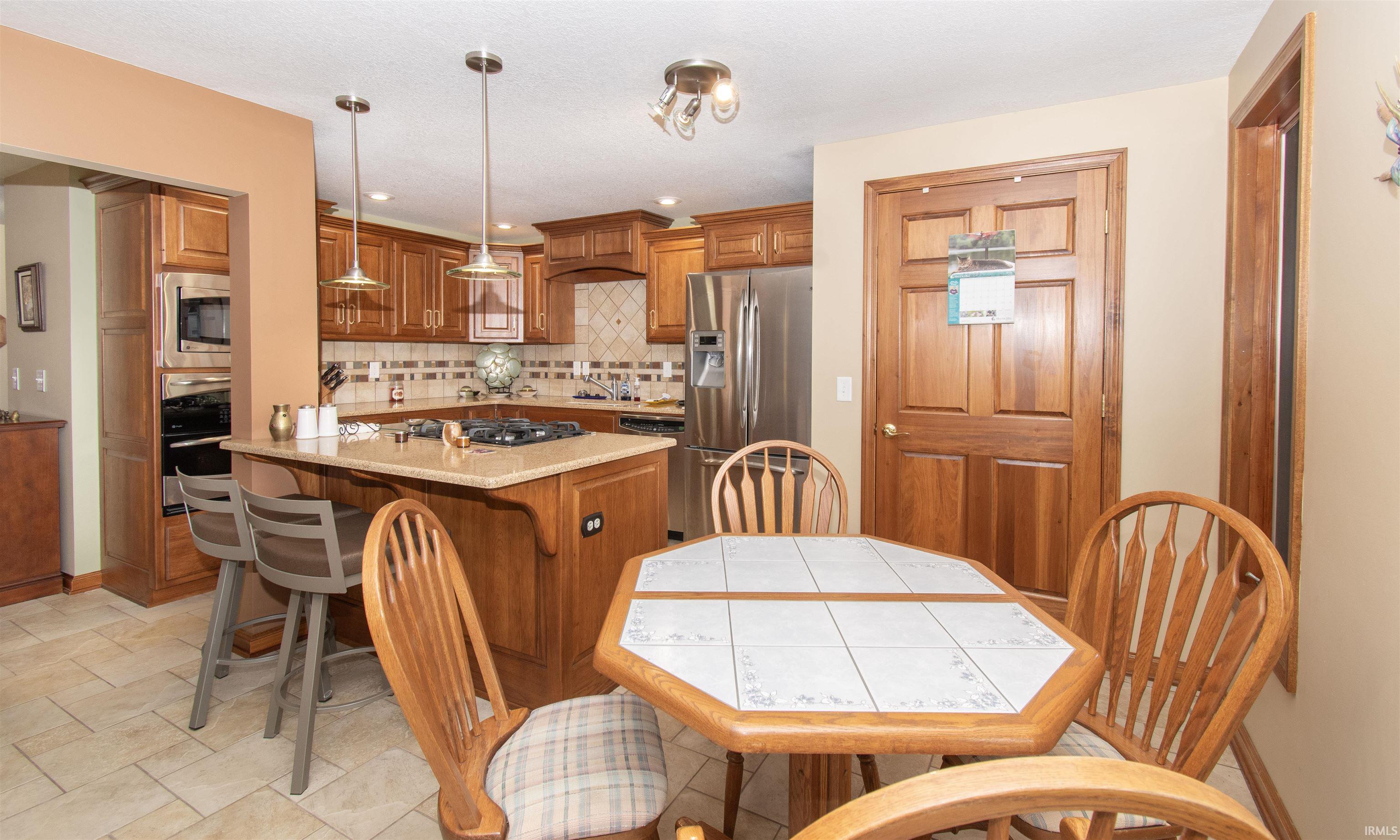 Kitchen featuring wood cabinetry, stainless steel appliances, a center island with pendant lighting, and a tile backsplash