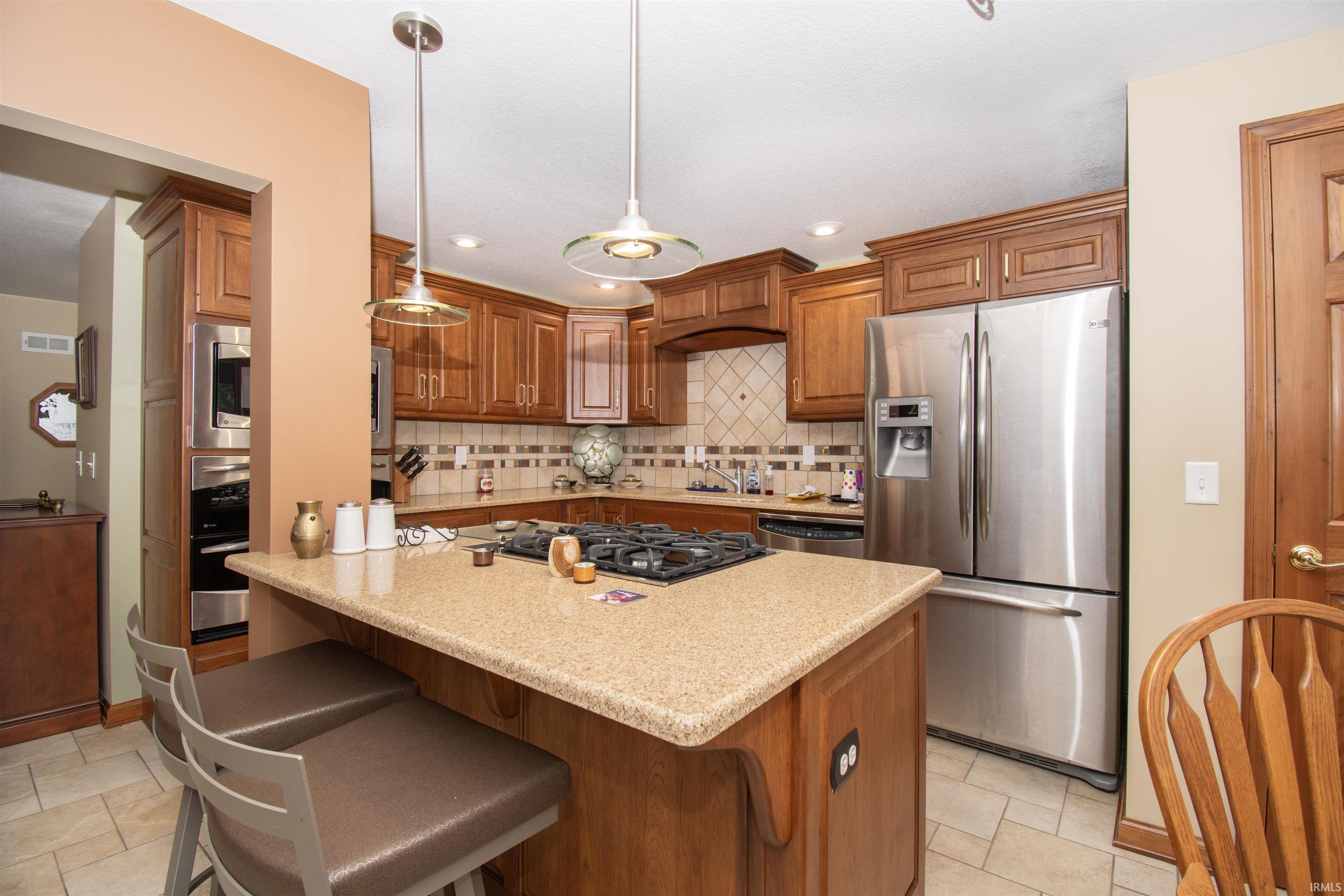 Kitchen featuring wood cabinetry, stainless steel appliances, a center island with a gas cooktop, pendant lighting, and tiled flooring