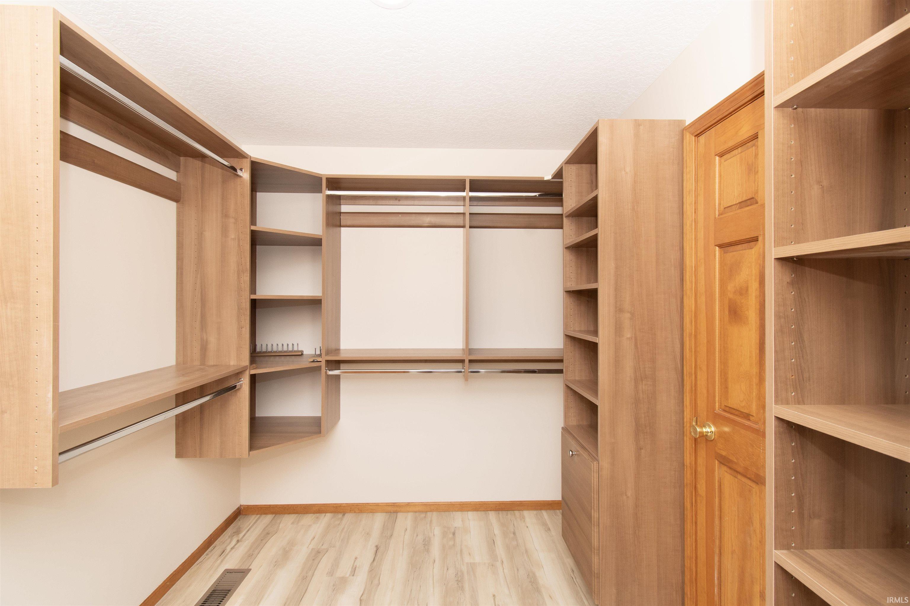 Custom wood-finish closet system featuring extensive shelving, multiple hanging rods, corner storage, and built-in drawers