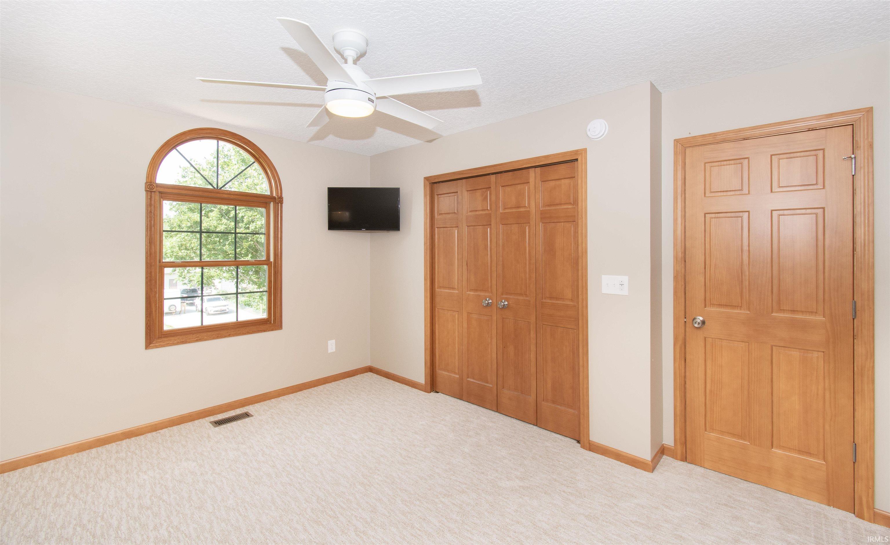 Carpeted room featuring a white ceiling fan with integrated lighting, an arched-top window with wood trim, wood-finish bi-fold closet doors, and a paneled wood-finish door