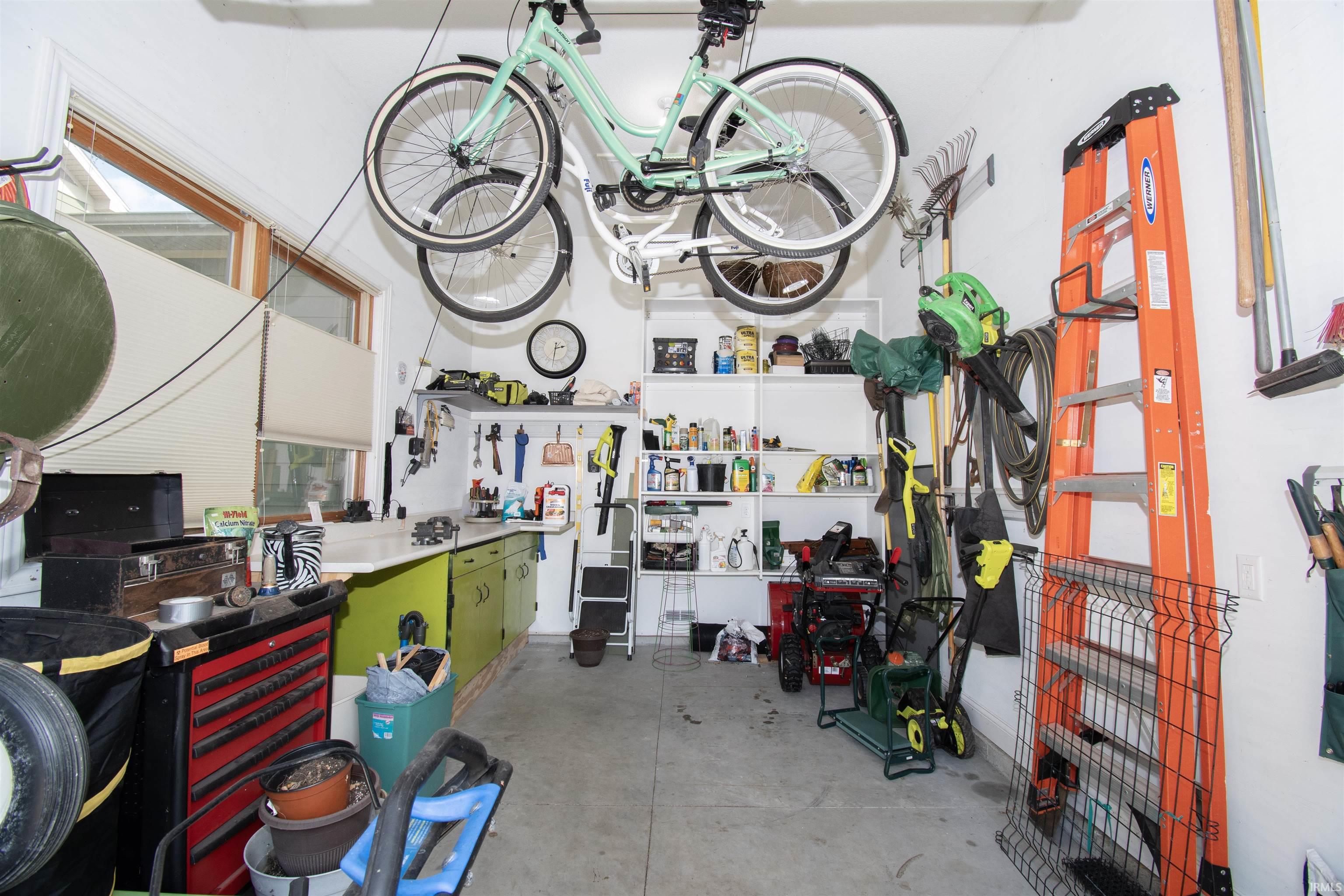 Attached garage featuring concrete flooring, built-in shelving, mounted tool storage, and a workbench with integrated cabinetry