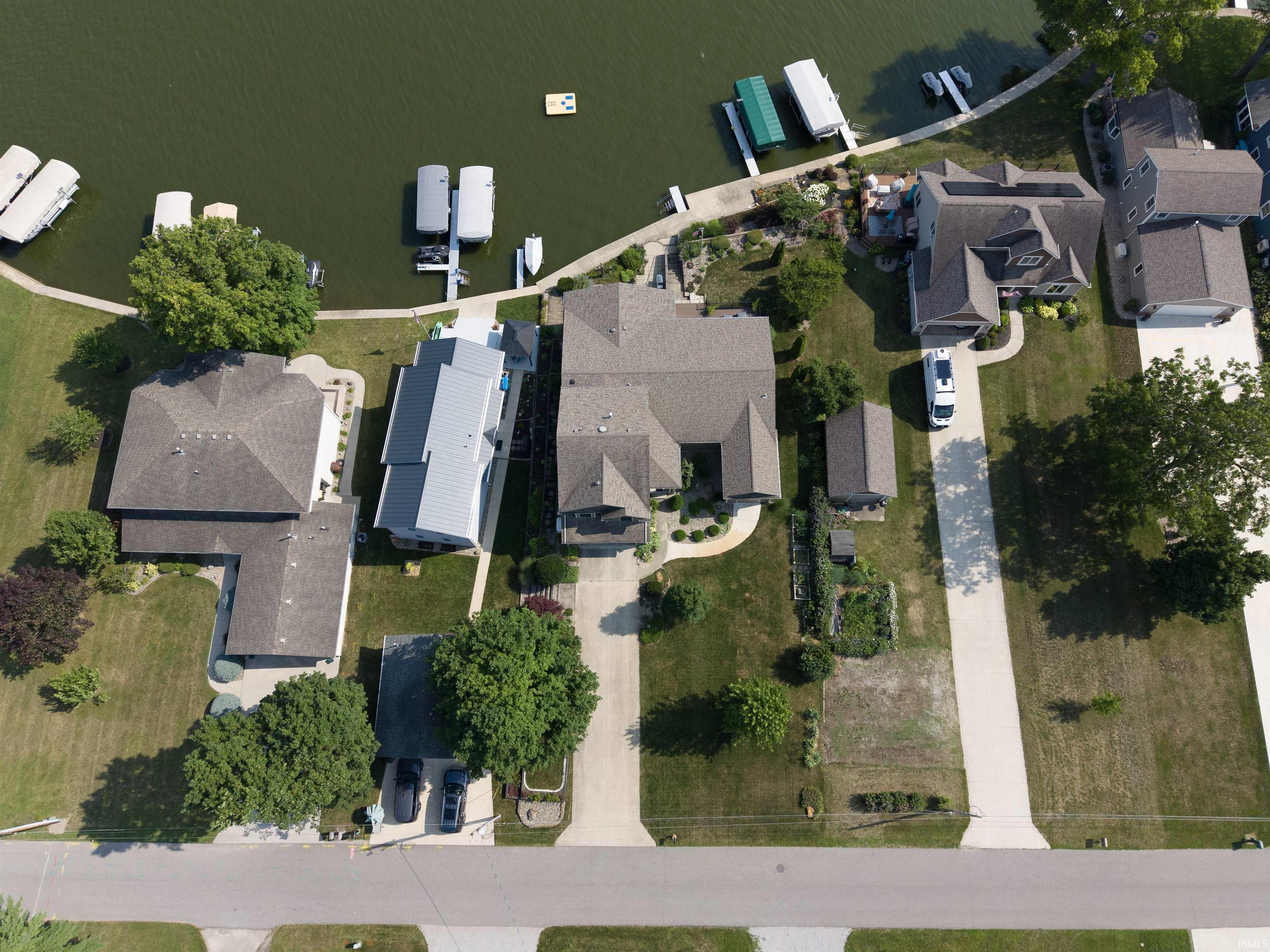 Waterfront property featuring a private boat dock, manicured lawn, paved driveway, mature trees, and a spacious backyard