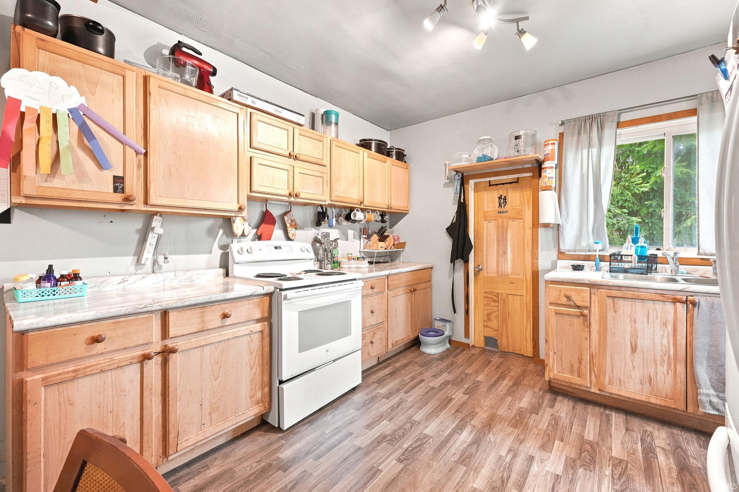 Kitchen featuring wood-finish flooring, light wood cabinetry, white countertops, a white electric range, and a window with natural light