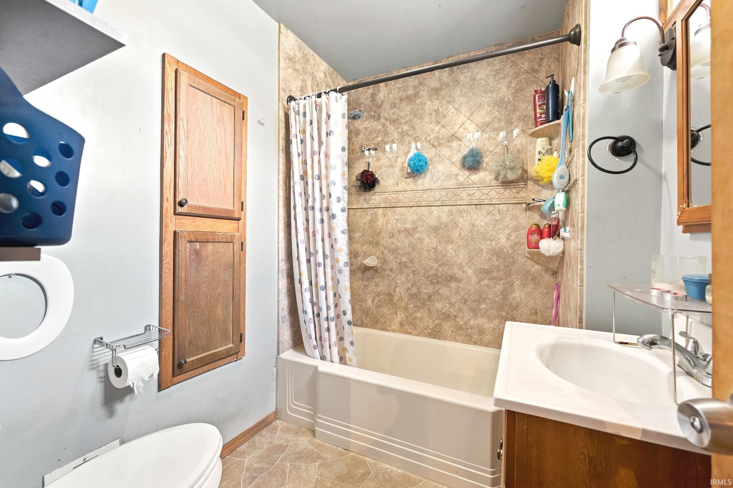 Full bathroom featuring a single vanity, a bathtub with an integrated shower, and a built-in wooden cabinet