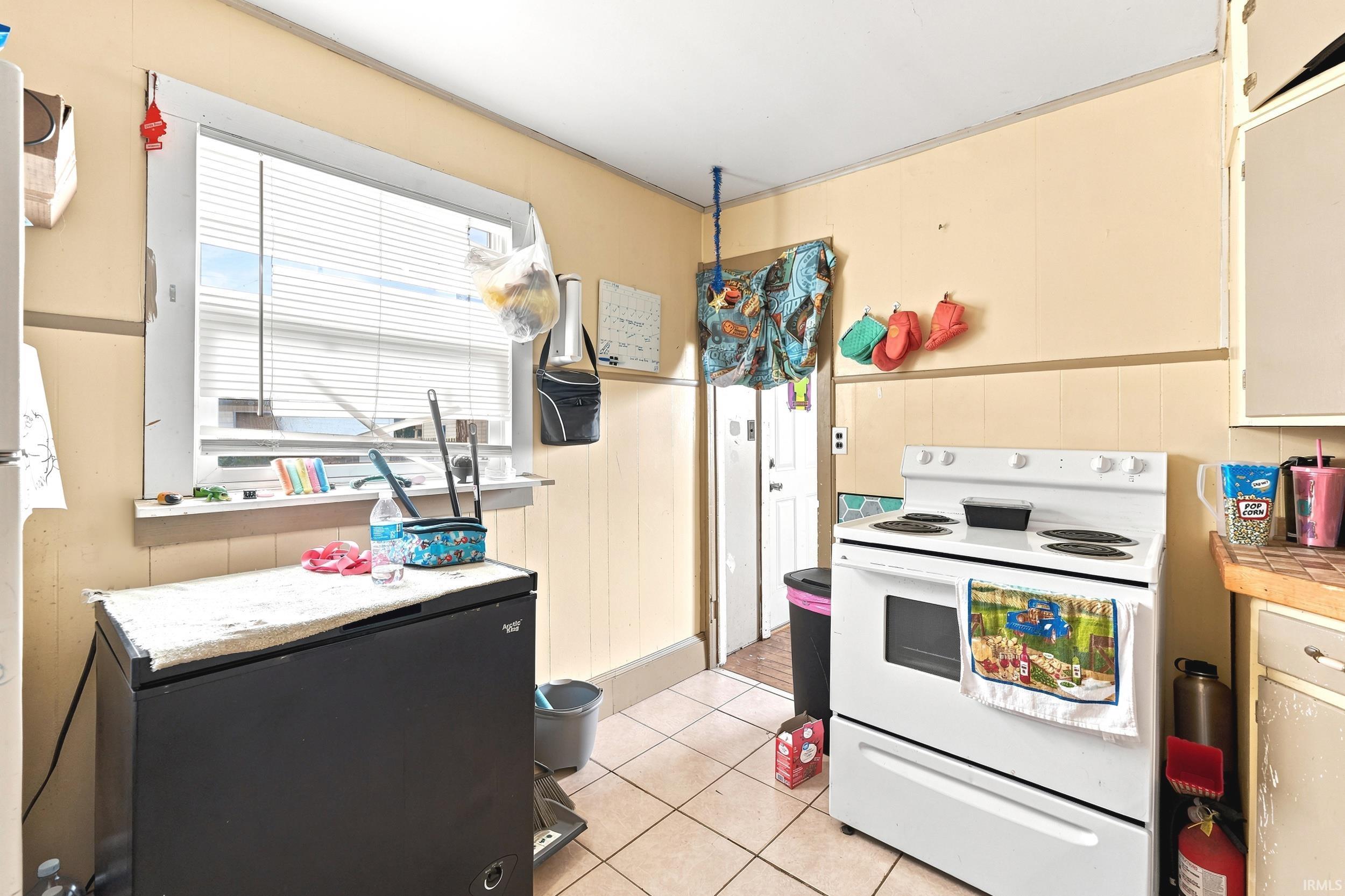 Kitchen space with tile flooring, a window featuring horizontal blinds, and a white freestanding electric range