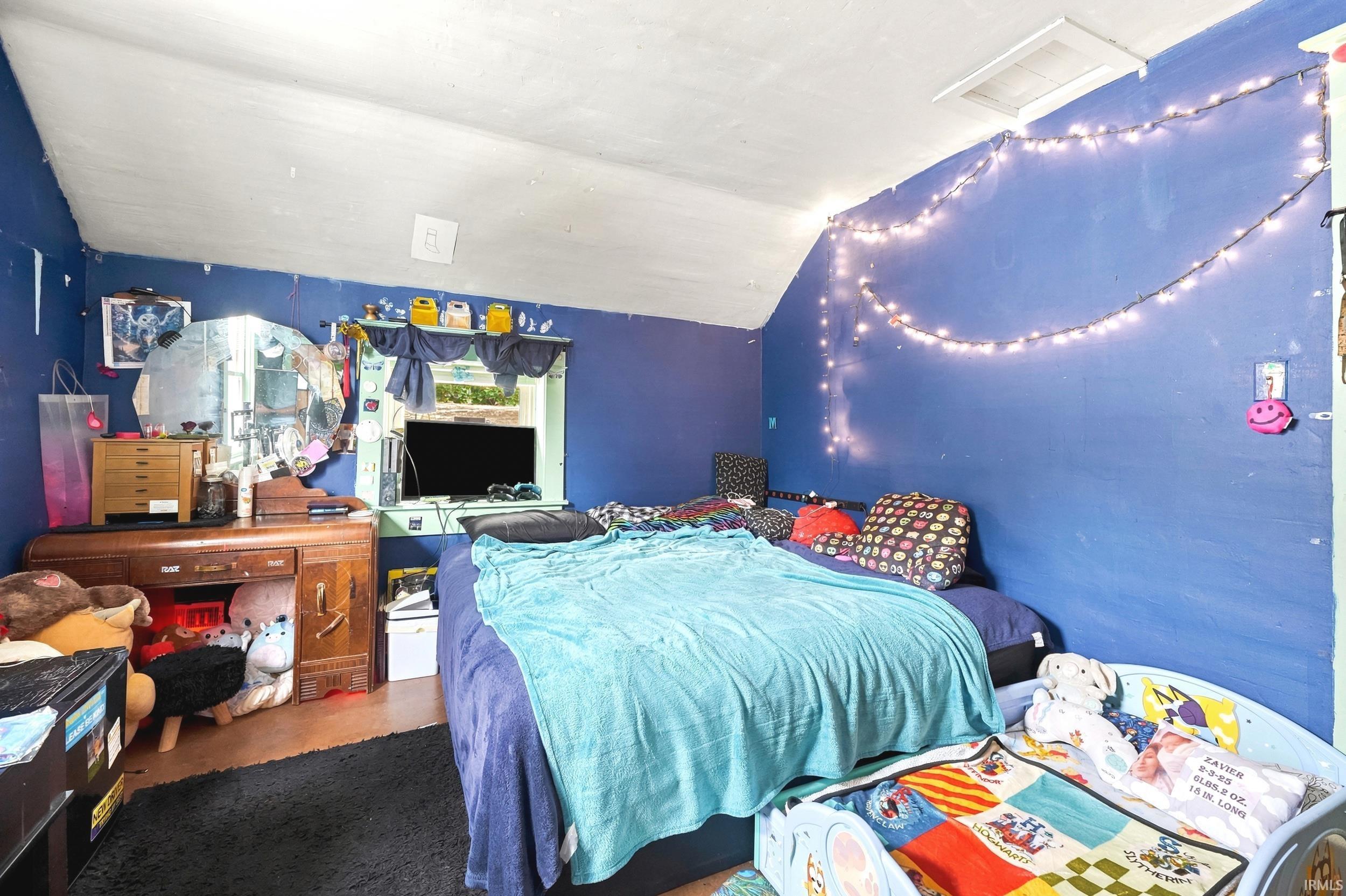 Sloped ceiling room featuring a window with exterior views and wood-finish flooring