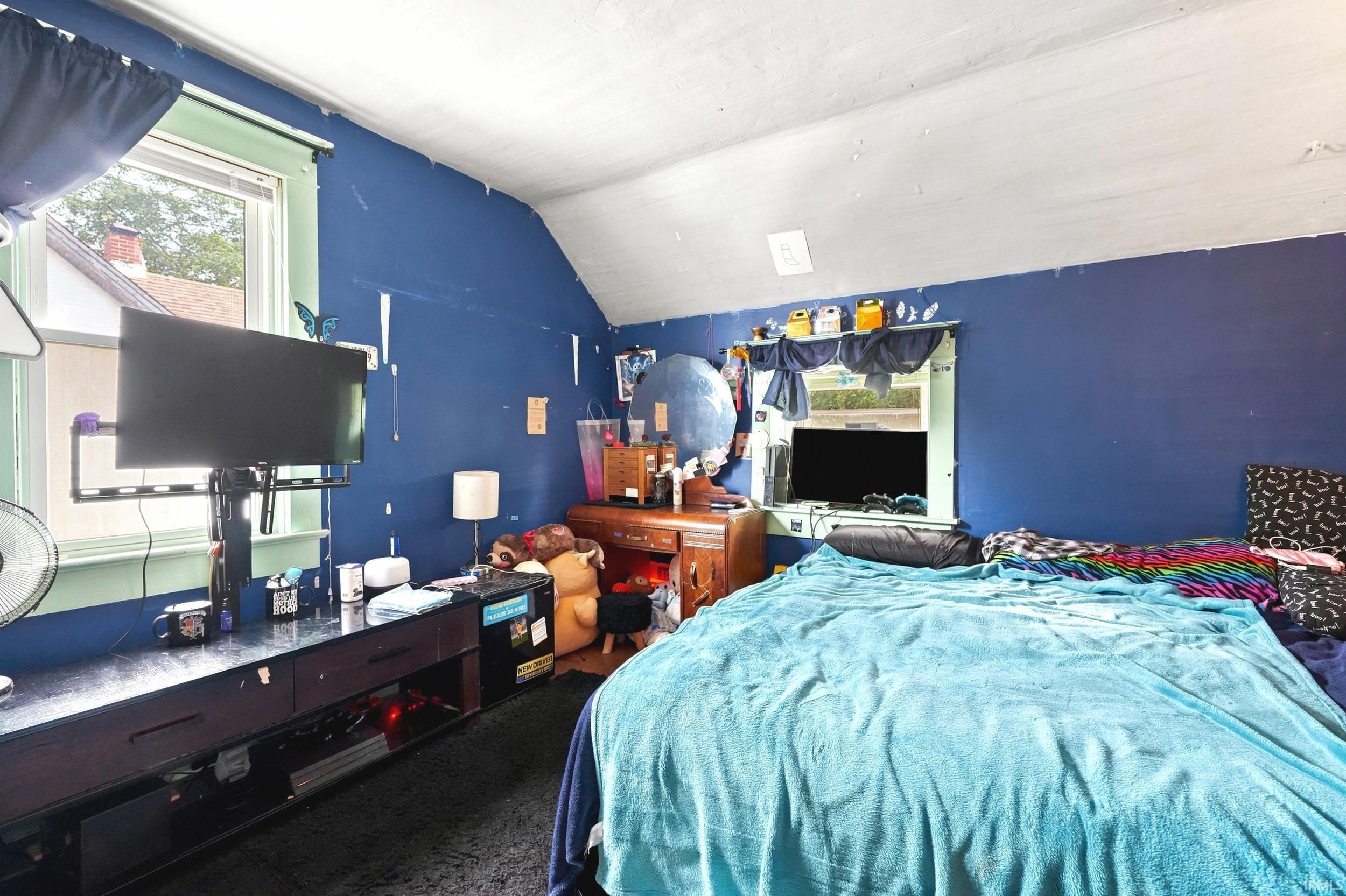 Room featuring an angled ceiling, window with light green trim, blue wall finish, and dark flooring
