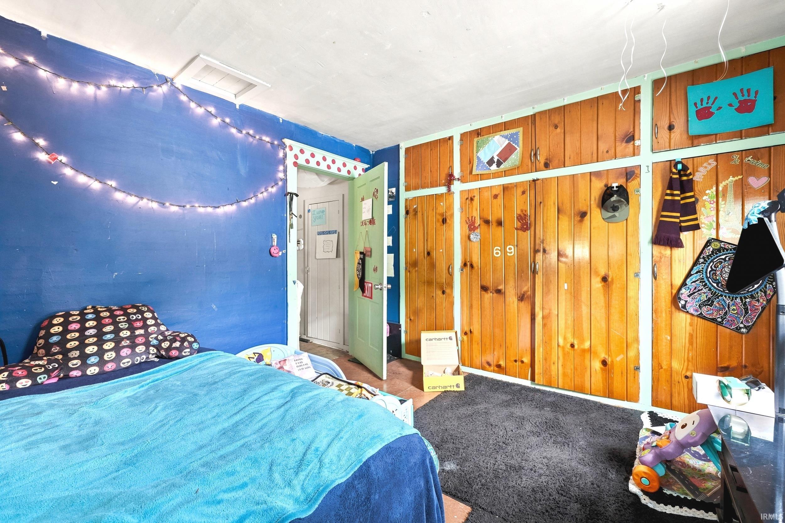 Interior room with wood-paneled wall, blue painted wall, light-colored ceiling, and dark carpet flooring