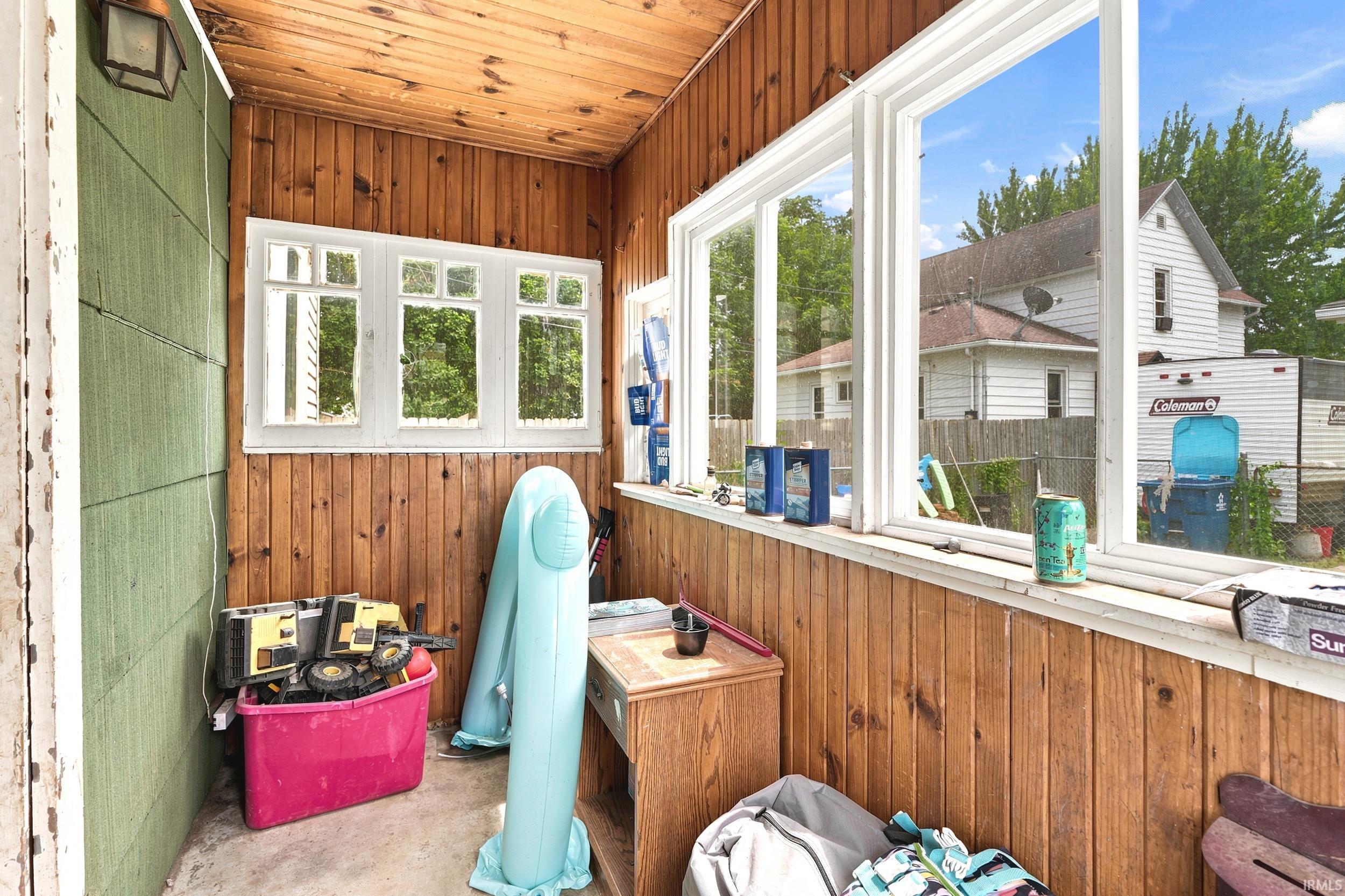 Enclosed porch featuring wood paneling on walls and ceiling, multiple windows, and an exterior wall light fixture