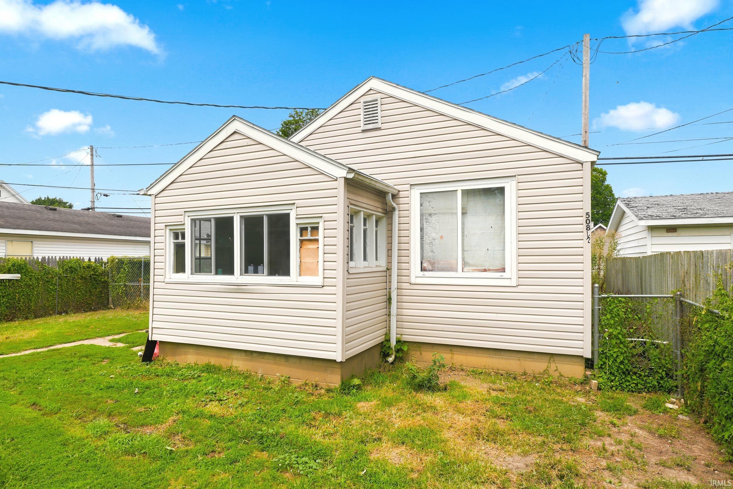 Light-toned siding exterior with white window trim and a partial chain-link fence