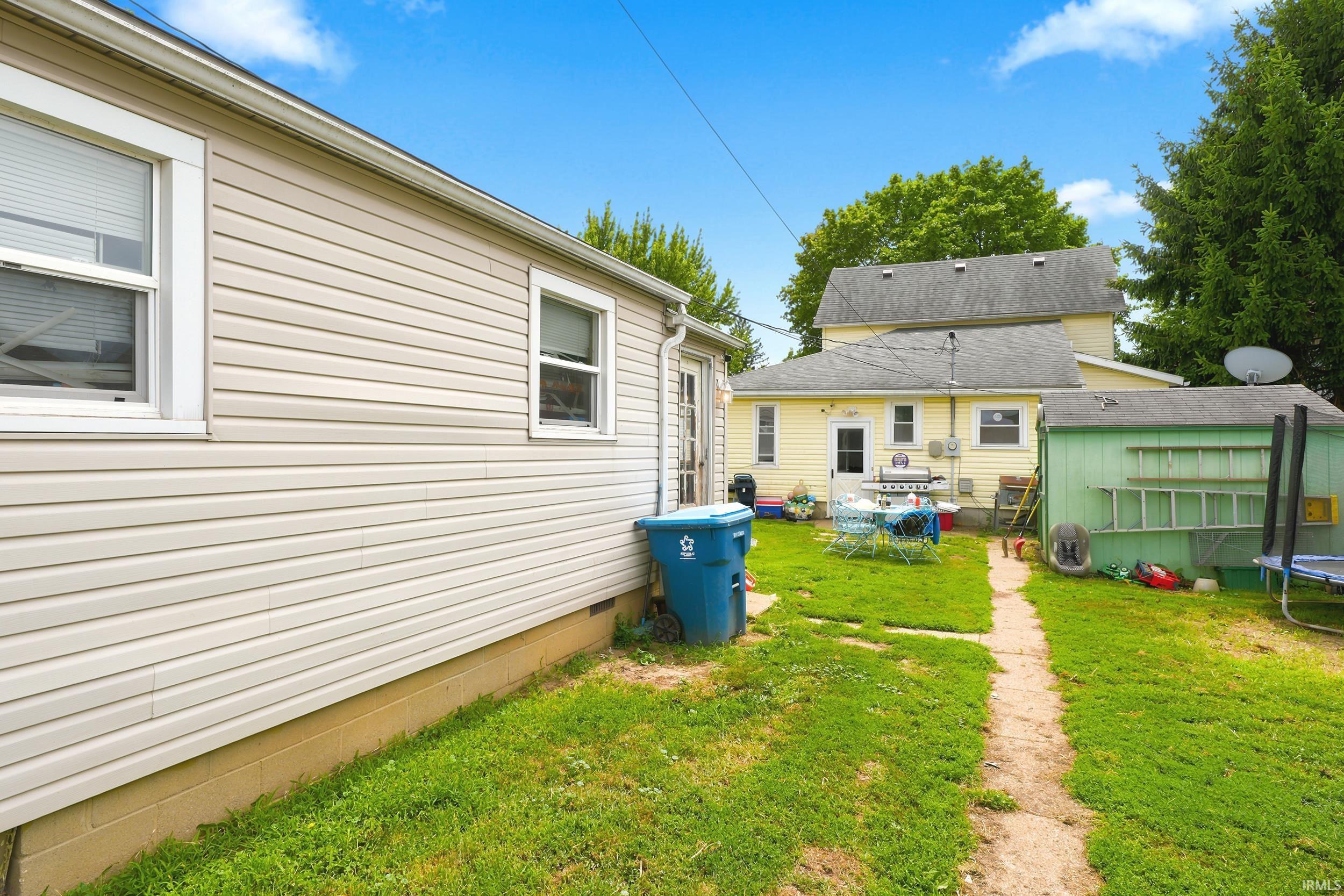 Rear exterior featuring a green storage shed, light yellow siding, and a partial view of a second structure