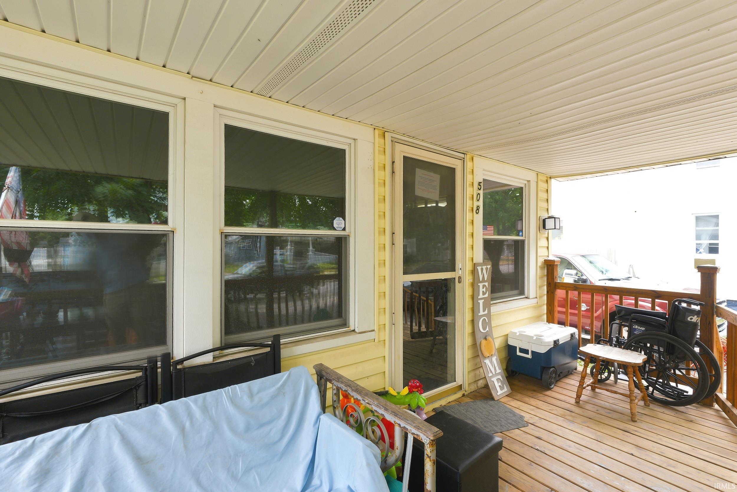 Covered porch with wood-finish decking, white vinyl siding, and multiple windows