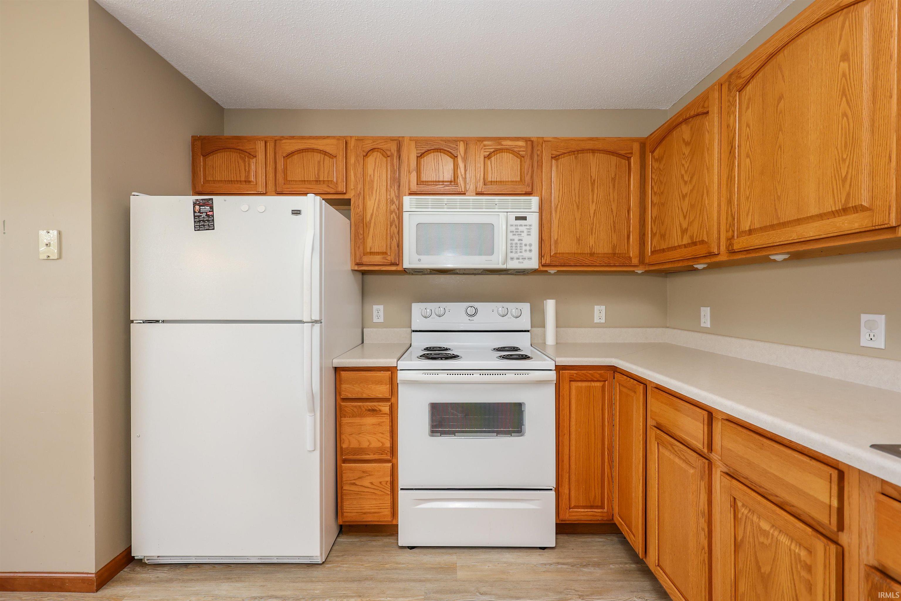 Kitchen featuring wood cabinetry, white appliances including a refrigerator, range, and microwave, and light-toned countertops