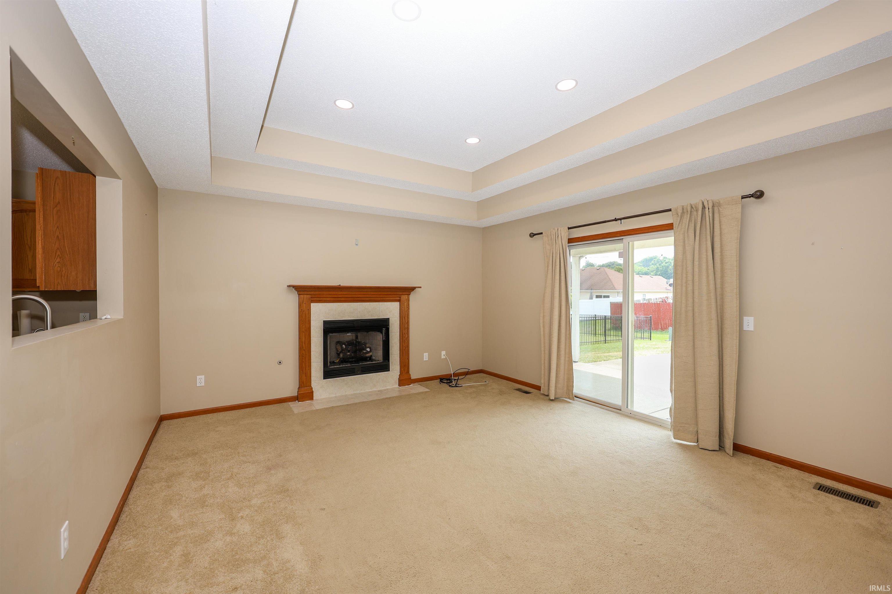 Living space featuring a tray ceiling with recessed lighting, a wood-surround fireplace with a hearth, and a sliding glass door to the exterior