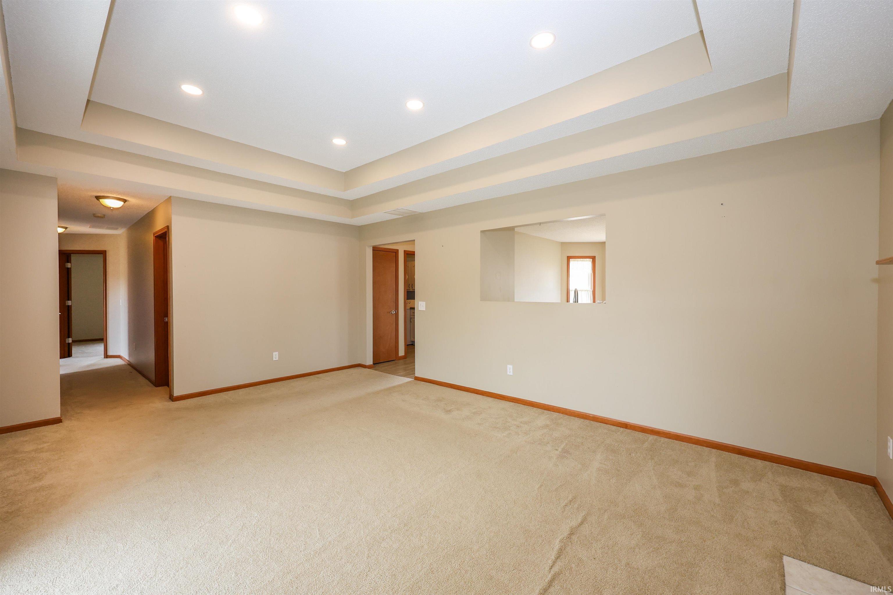 Recessed lighting illuminates the tray ceiling, complementing the neutral wall tones and light-colored carpeting