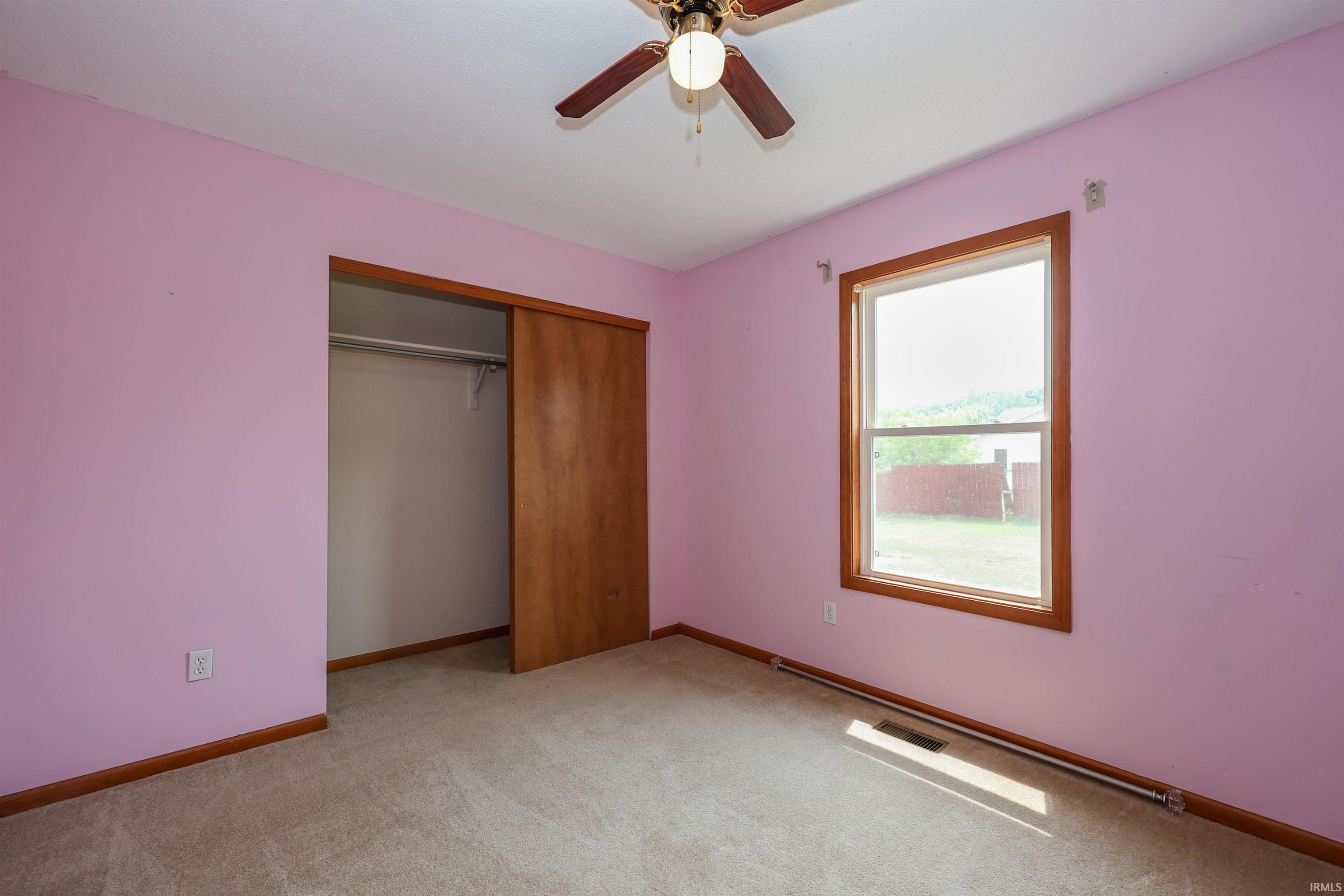 Carpeted room featuring a ceiling fan with light fixture, wood-trimmed window, and sliding closet doors