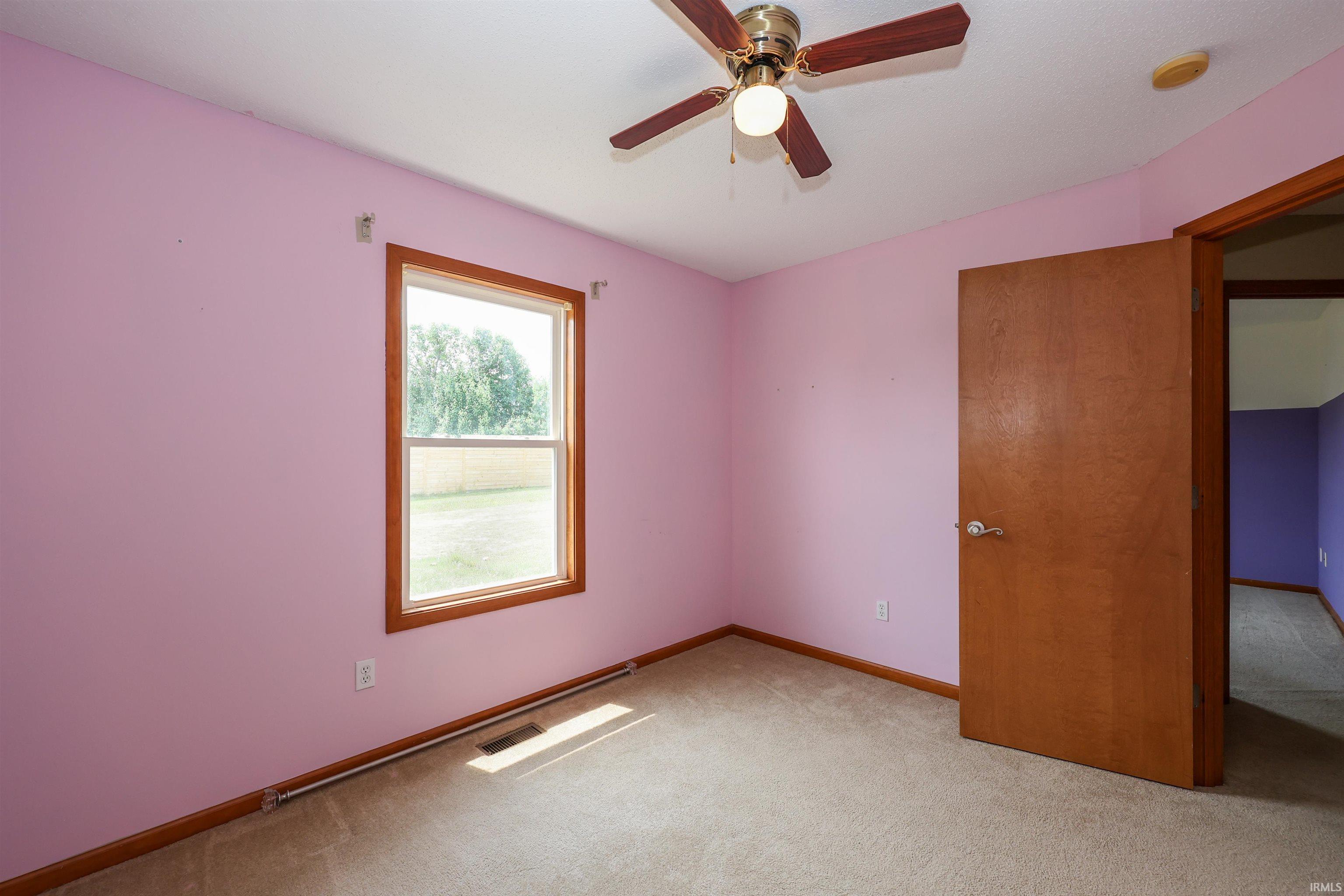Interior room featuring light-colored carpeting, a window with wood-finish trim, a paneled wood-finish door, and a ceiling fan with light fixture