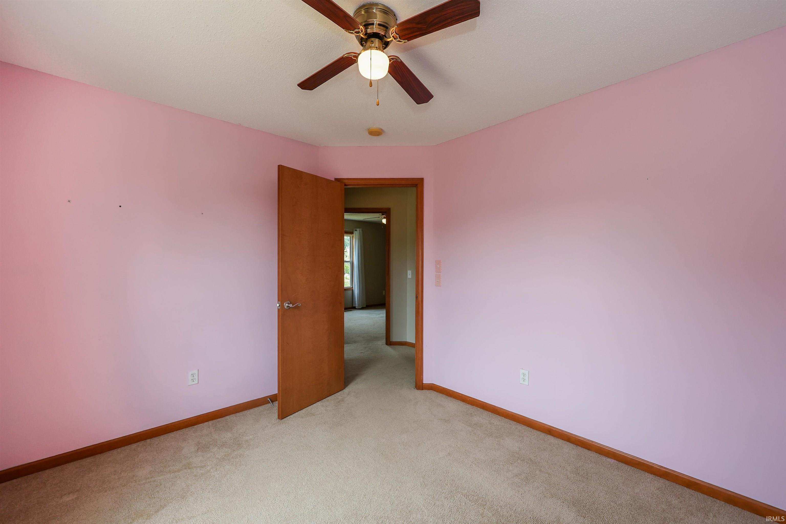 Carpeted room featuring a ceiling fan with light fixture, wood-finish baseboards, and a wood-finish door with brushed nickel hardware