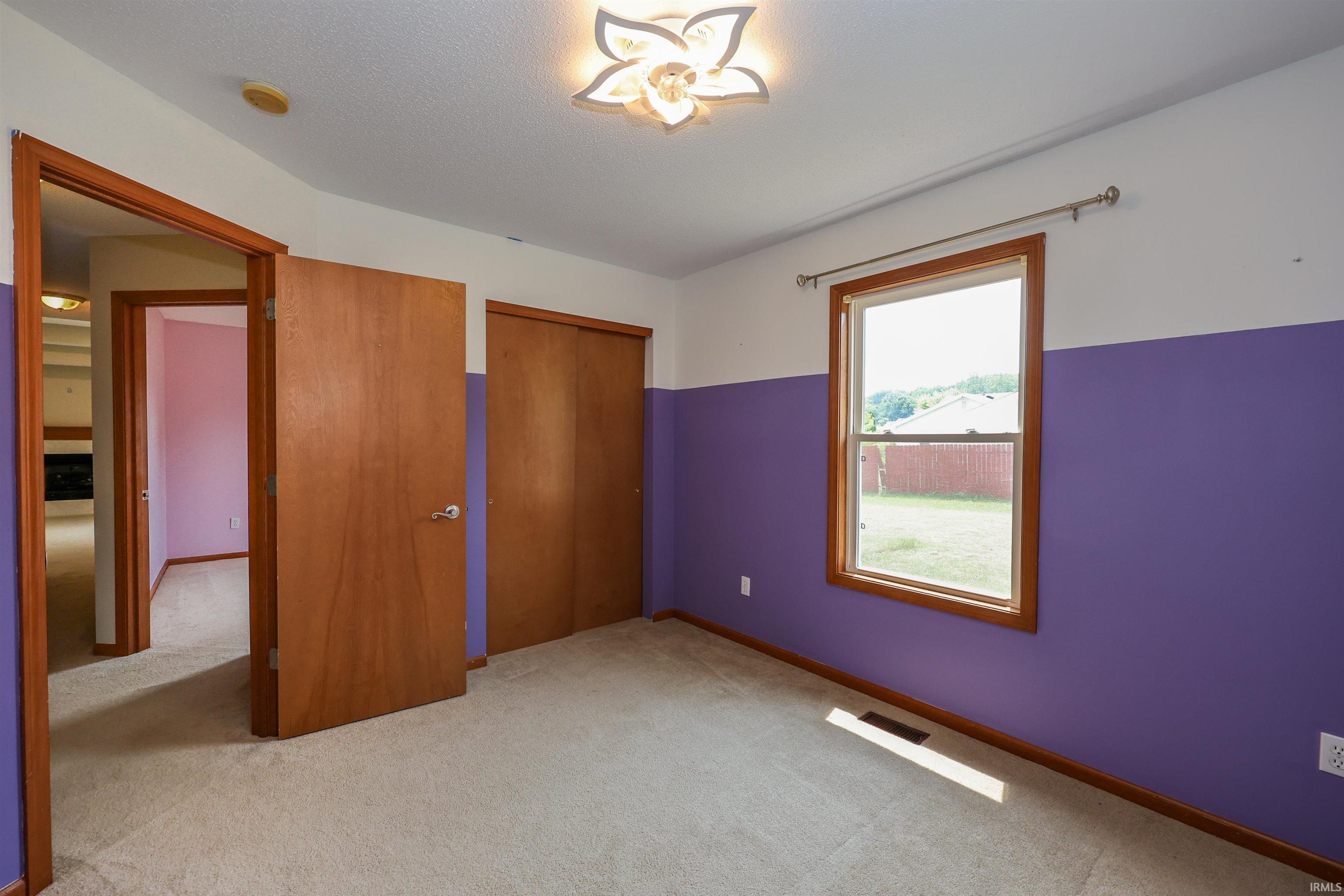 Carpeted interior room featuring a window with wood trim, two wood-paneled closet doors, and a wood-paneled entry door