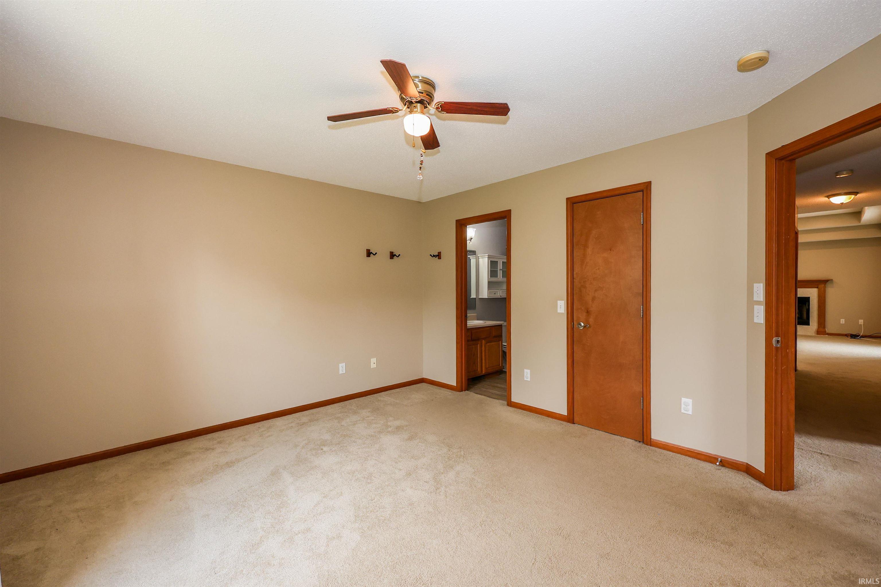 Carpeted room with neutral wall tones, featuring a ceiling fan with light fixture, wood trim, and multiple doorways