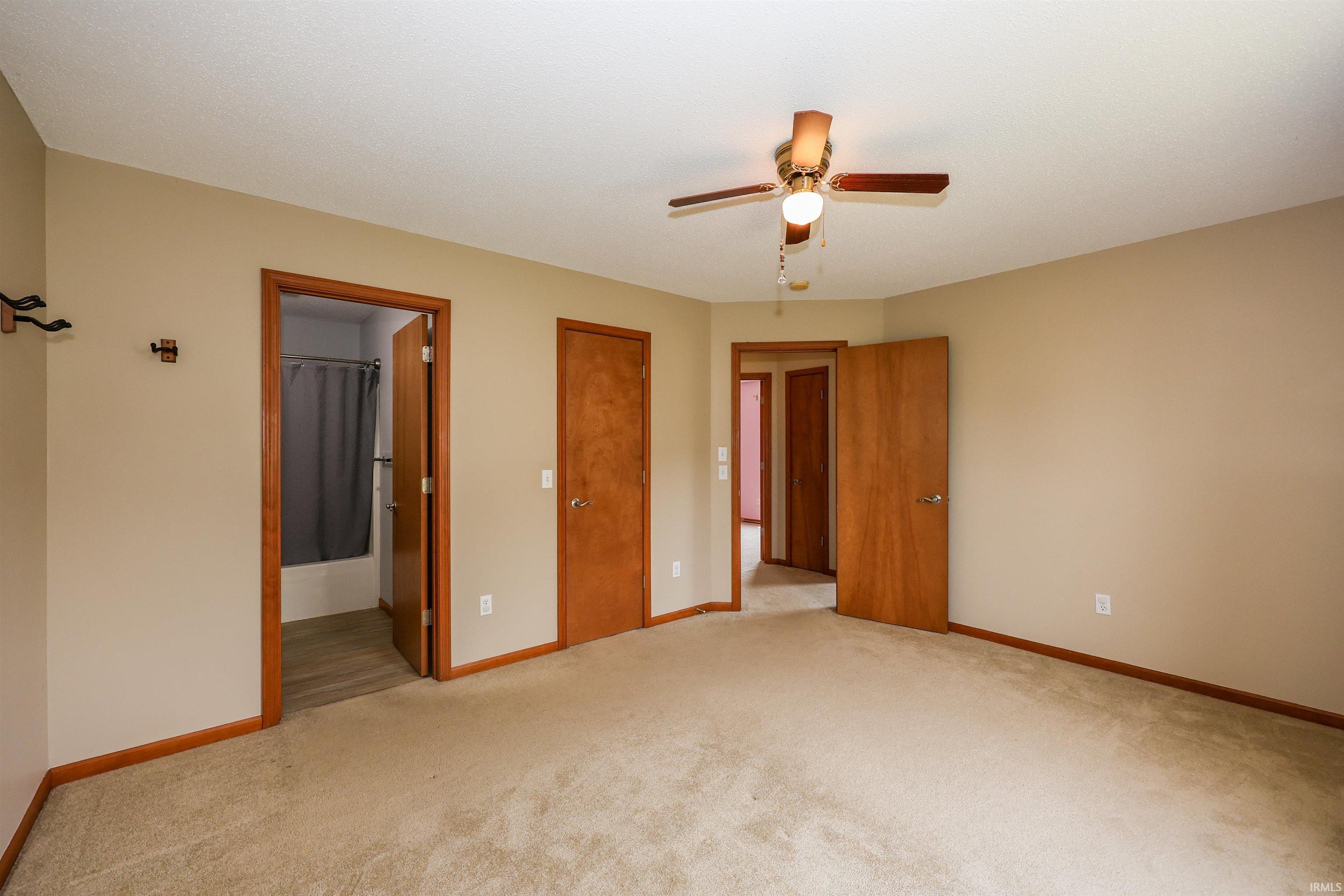 Carpeted room featuring a ceiling fan with integrated lighting, multiple wood-paneled doors, and light neutral wall paint