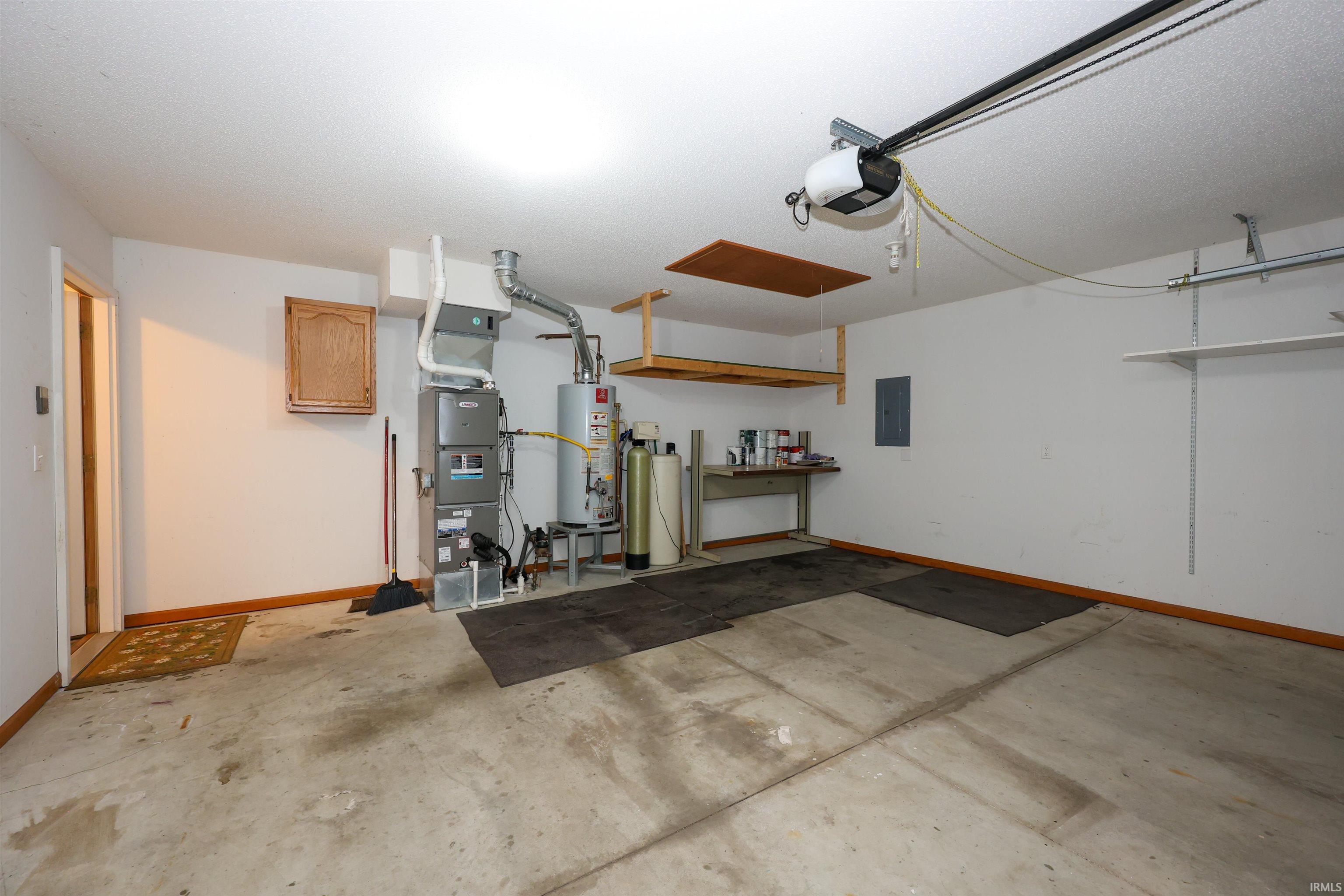 Spacious garage featuring a concrete floor, overhead storage shelves, built-in wall shelving, a wall-mounted wooden cabinet, and an automatic garage door opener