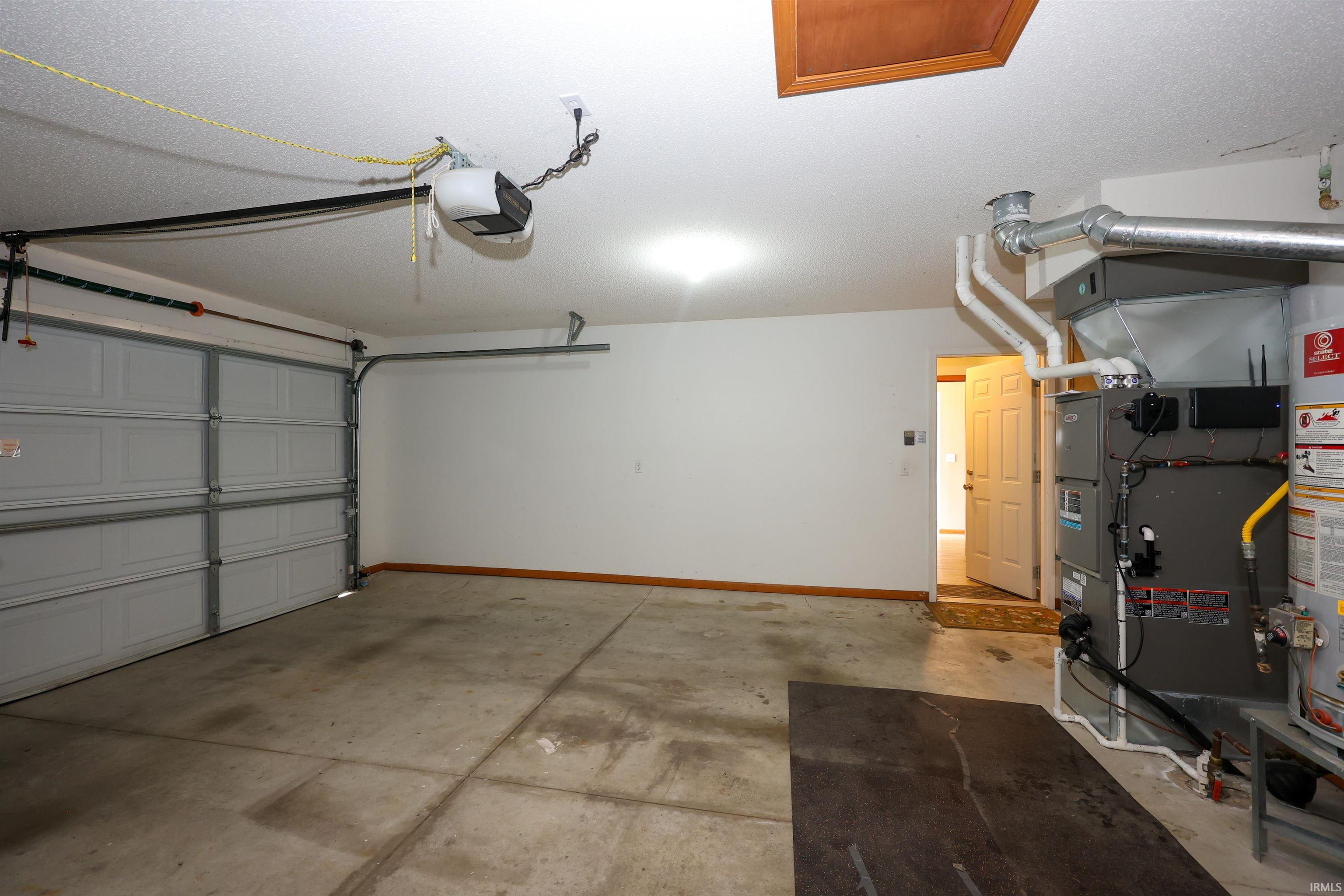 Spacious garage featuring a concrete floor, overhead garage door with opener, and dedicated utility area with water heater and furnace