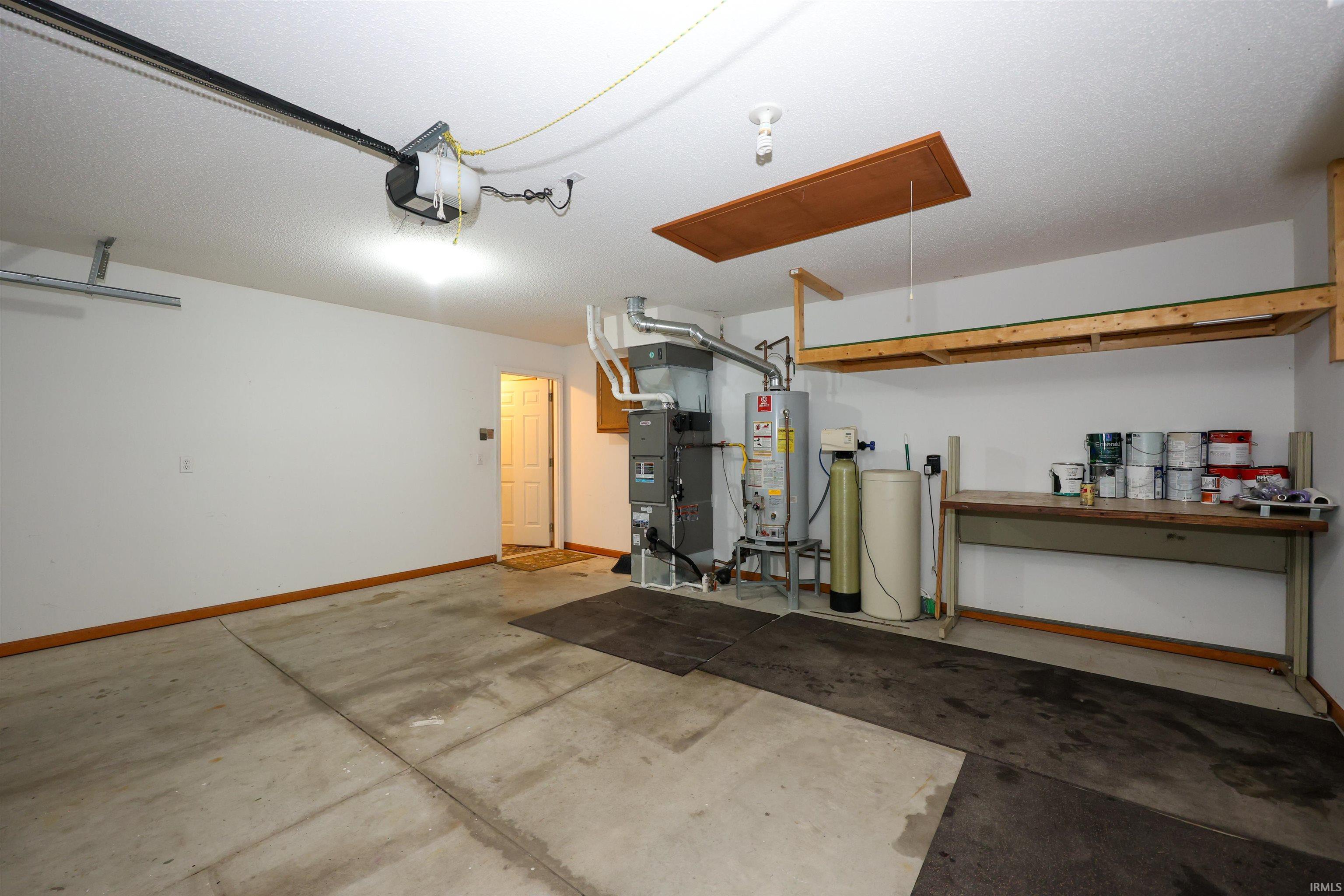 Attached garage featuring concrete flooring, built-in shelving, an overhead garage door opener, and integrated utilities