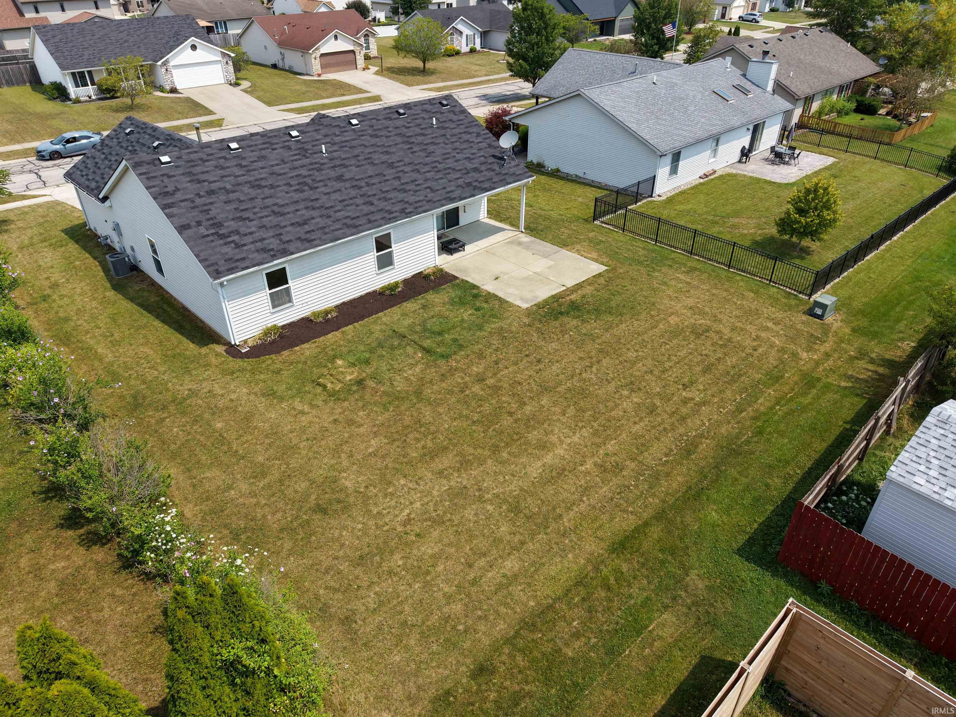 Expansive backyard with a concrete patio, mature landscaping, and a white siding exterior