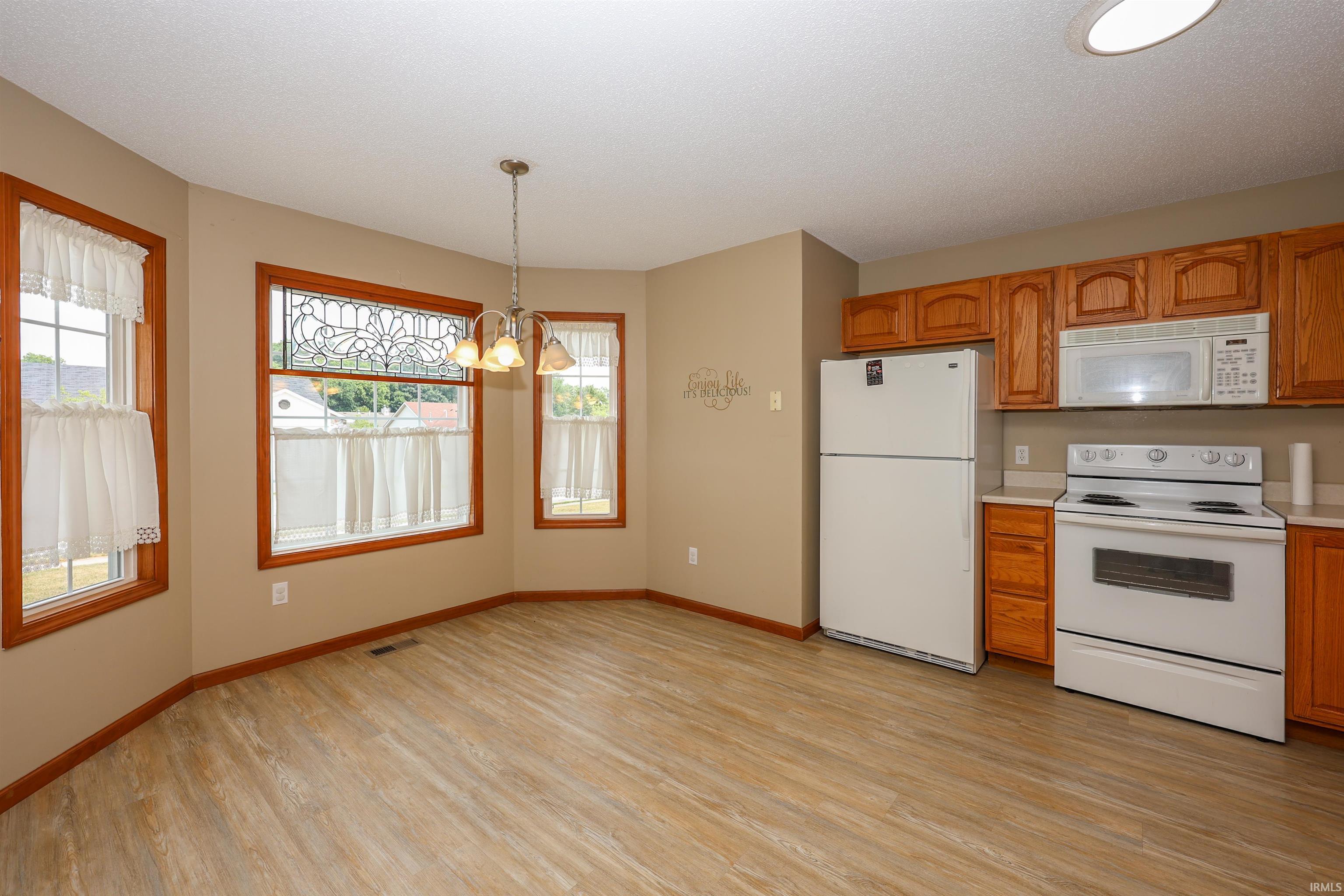 Eat-in kitchen featuring wood-finish flooring, a bay window with decorative glass, and a chandelier