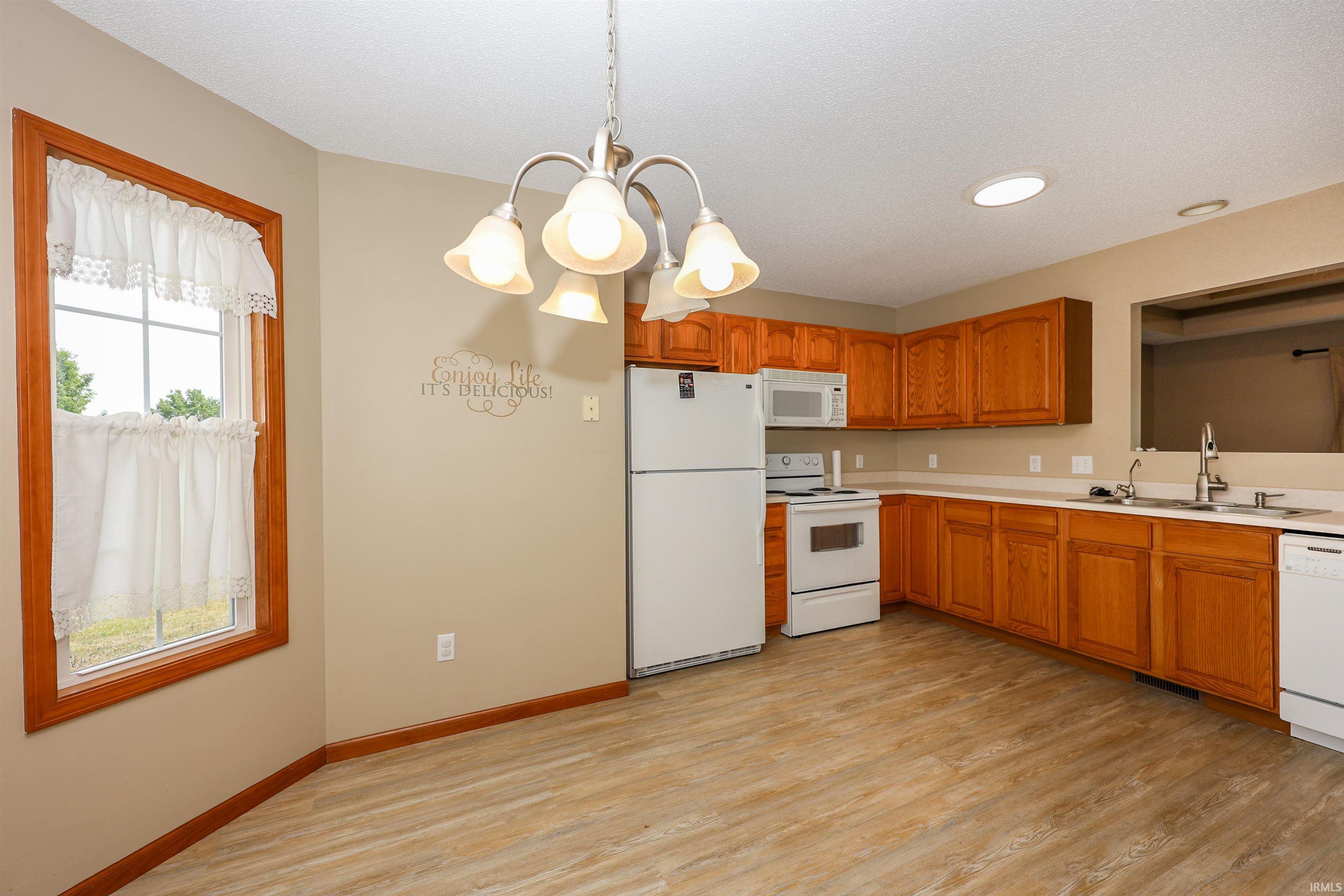 Eat-in kitchen featuring wood-finish flooring, ample cabinetry, white appliances, and a window with natural light