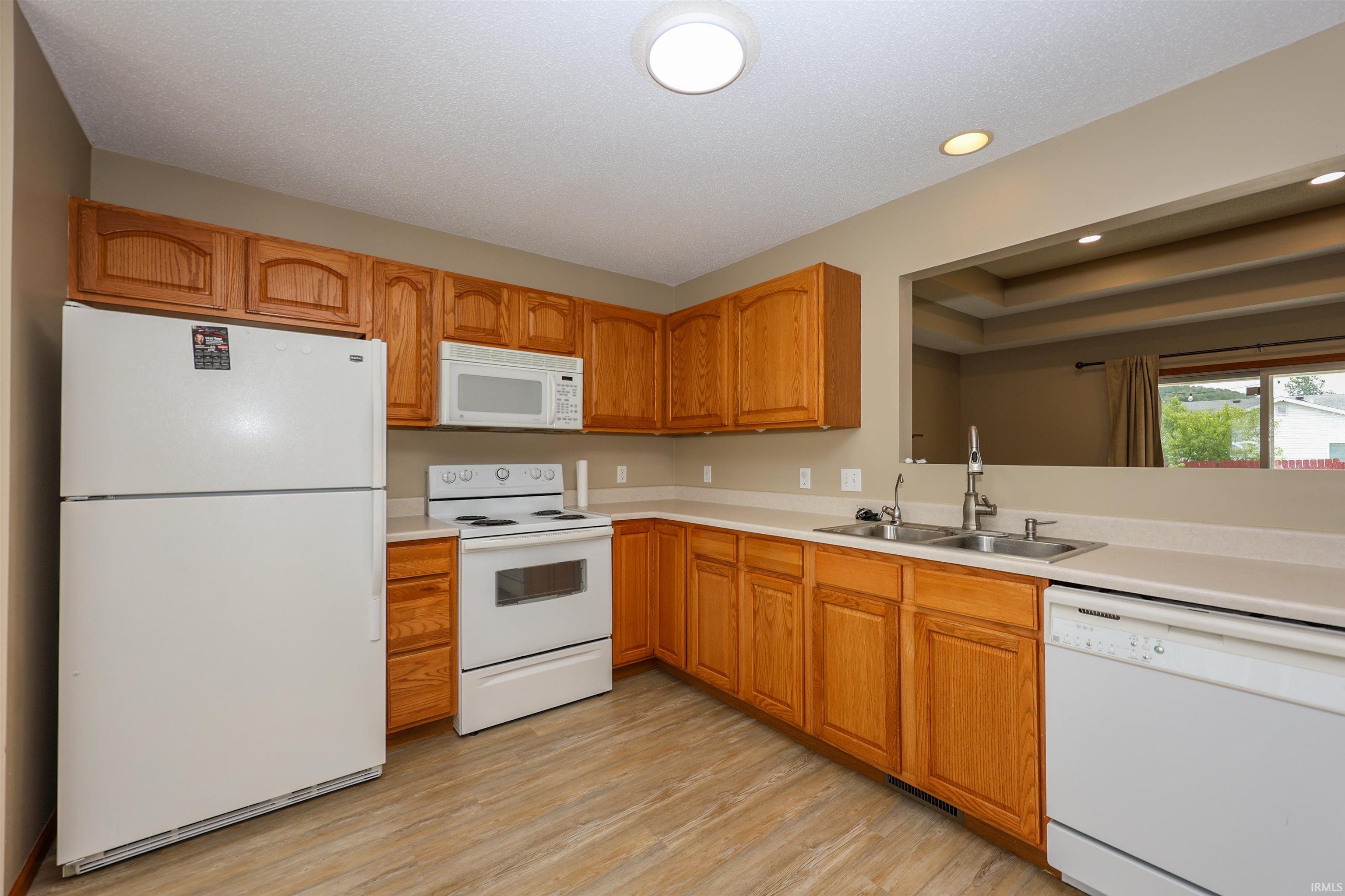 Kitchen featuring wood-finish cabinetry, light countertops, and white appliances including a refrigerator, range, microwave, and dishwasher