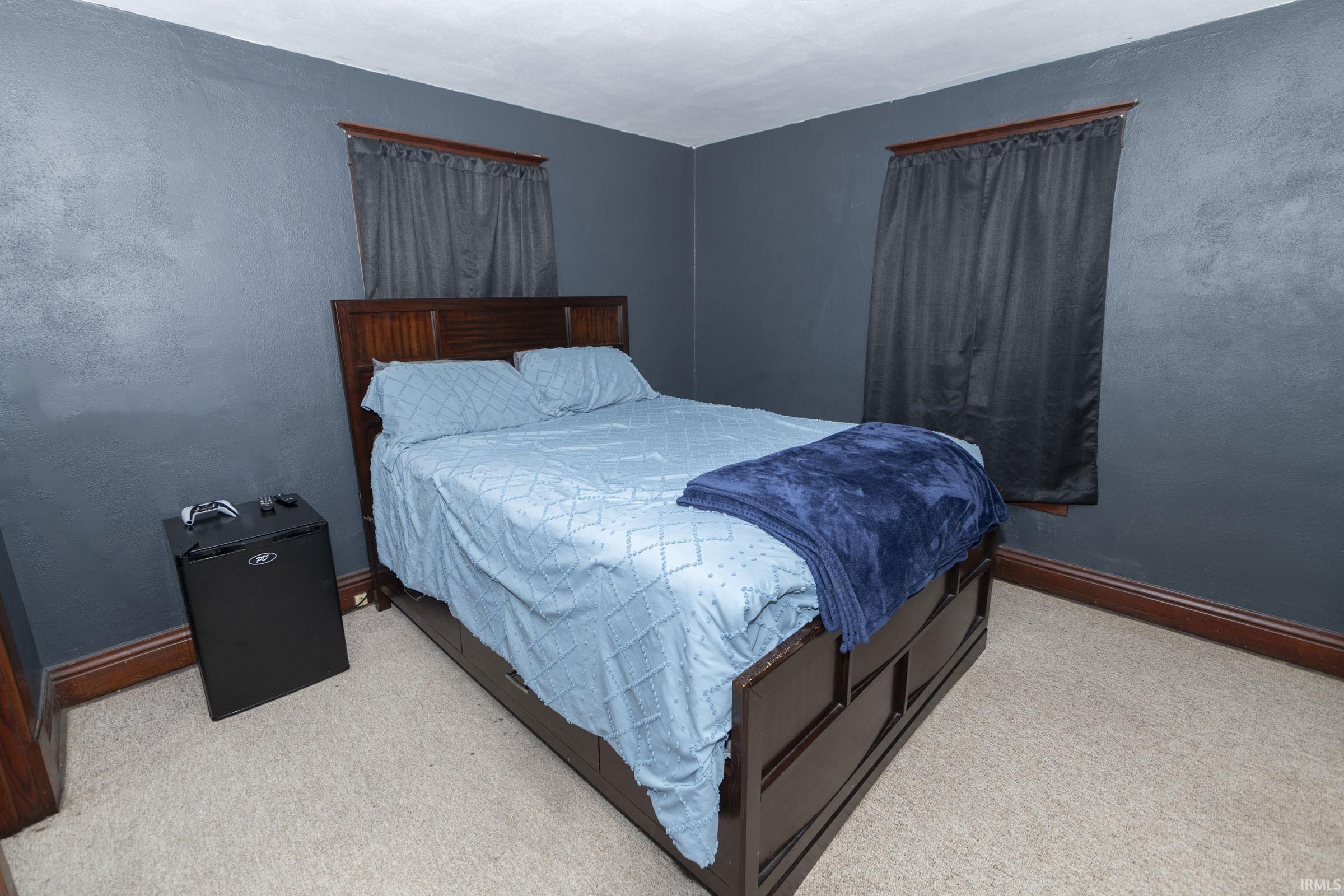 Carpeted room featuring dark walls, two windows with dark drapes, and rich wood-tone baseboards