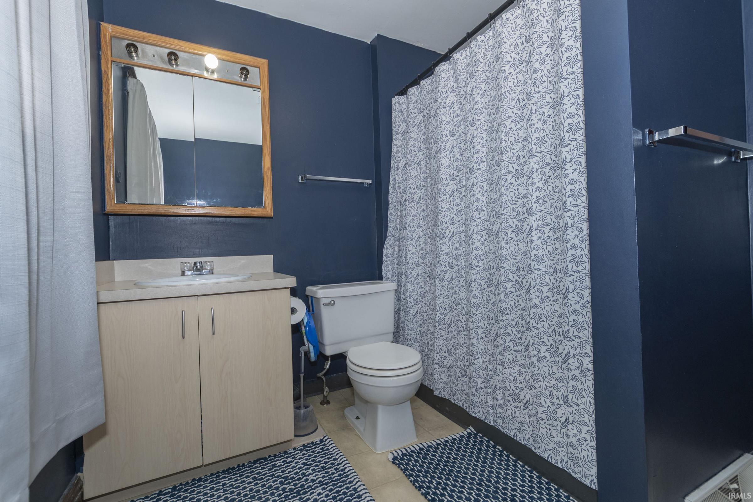 Bathroom featuring a light wood-finish vanity with a single sink and light countertop, accented by a wood-framed medicine cabinet with integrated lighting