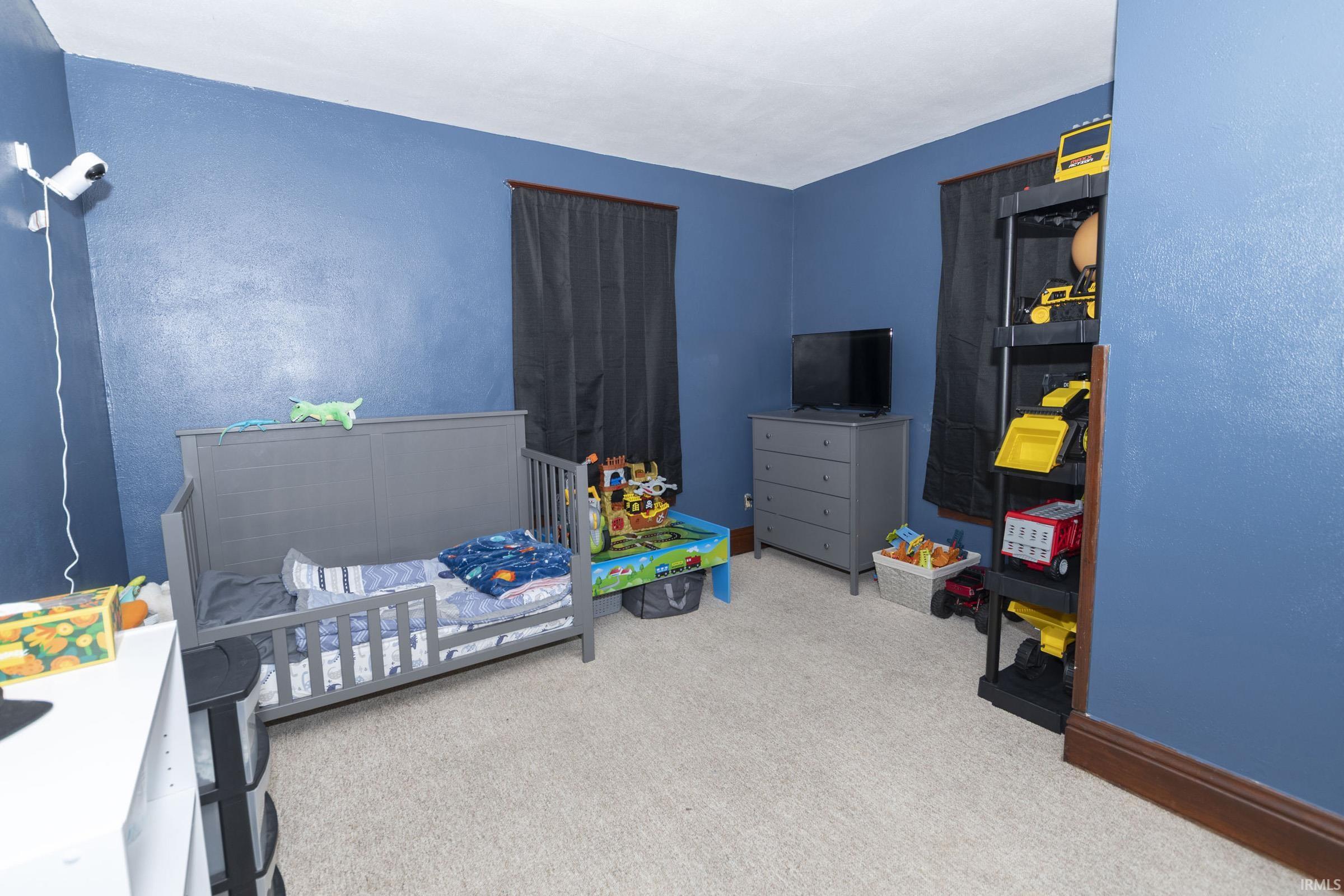 Interior room featuring blue wall paint, light-toned carpet flooring, and dark window coverings