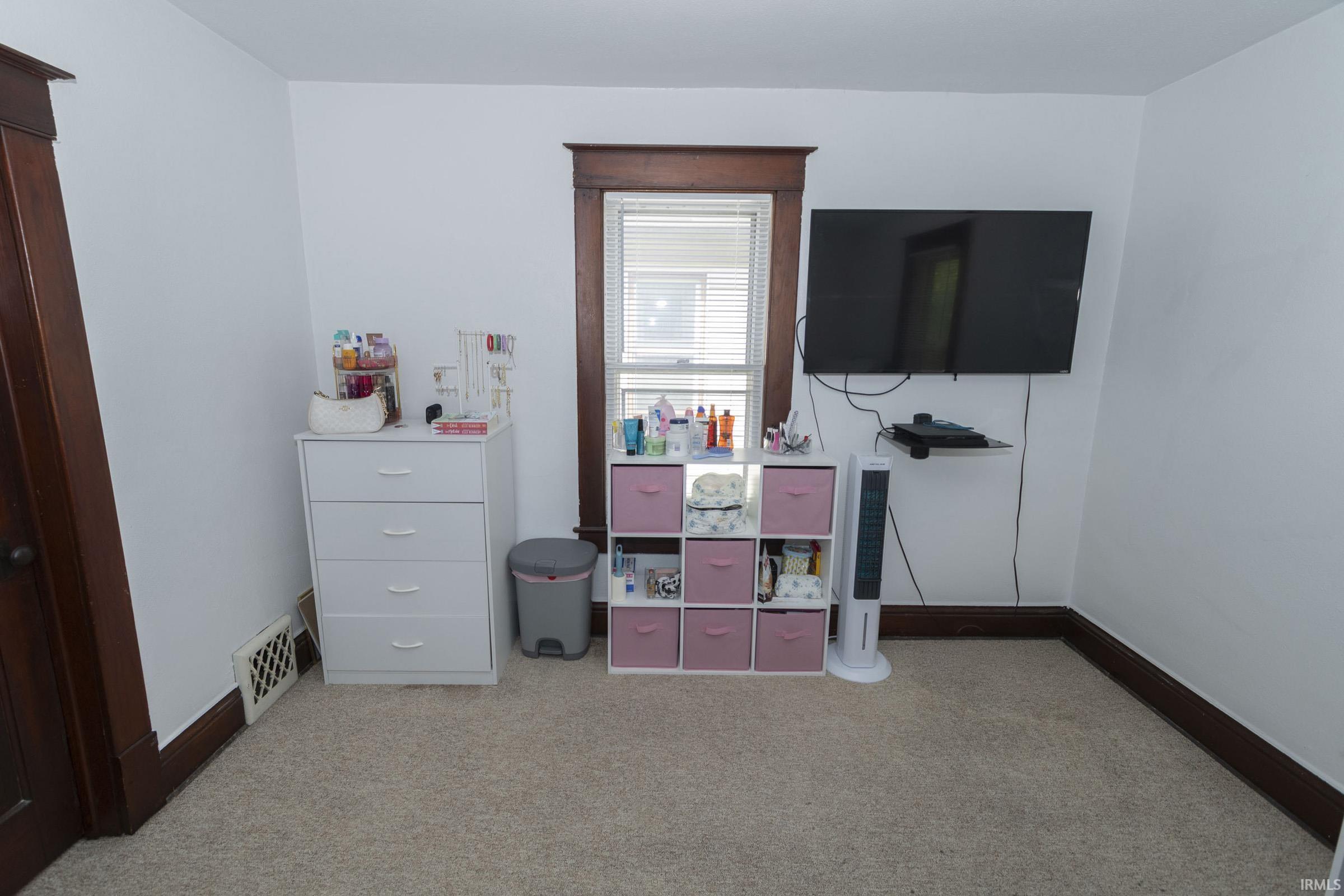 Carpeted room featuring a single window with blinds, dark wood trim, white walls, and a wall-mounted television bracket